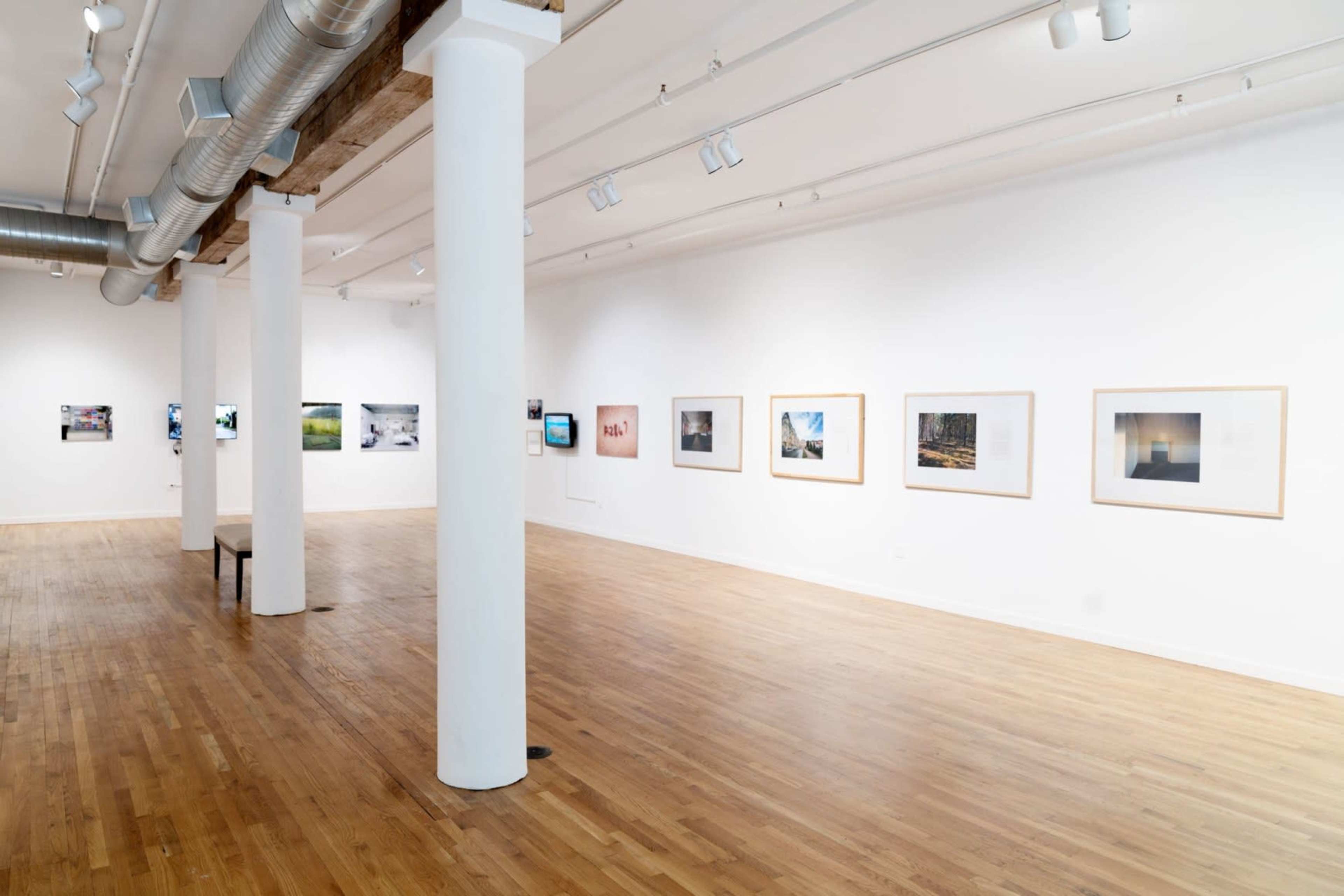 An art gallery features a series of framed photographs displayed along white walls with wooden flooring and a central bench.
