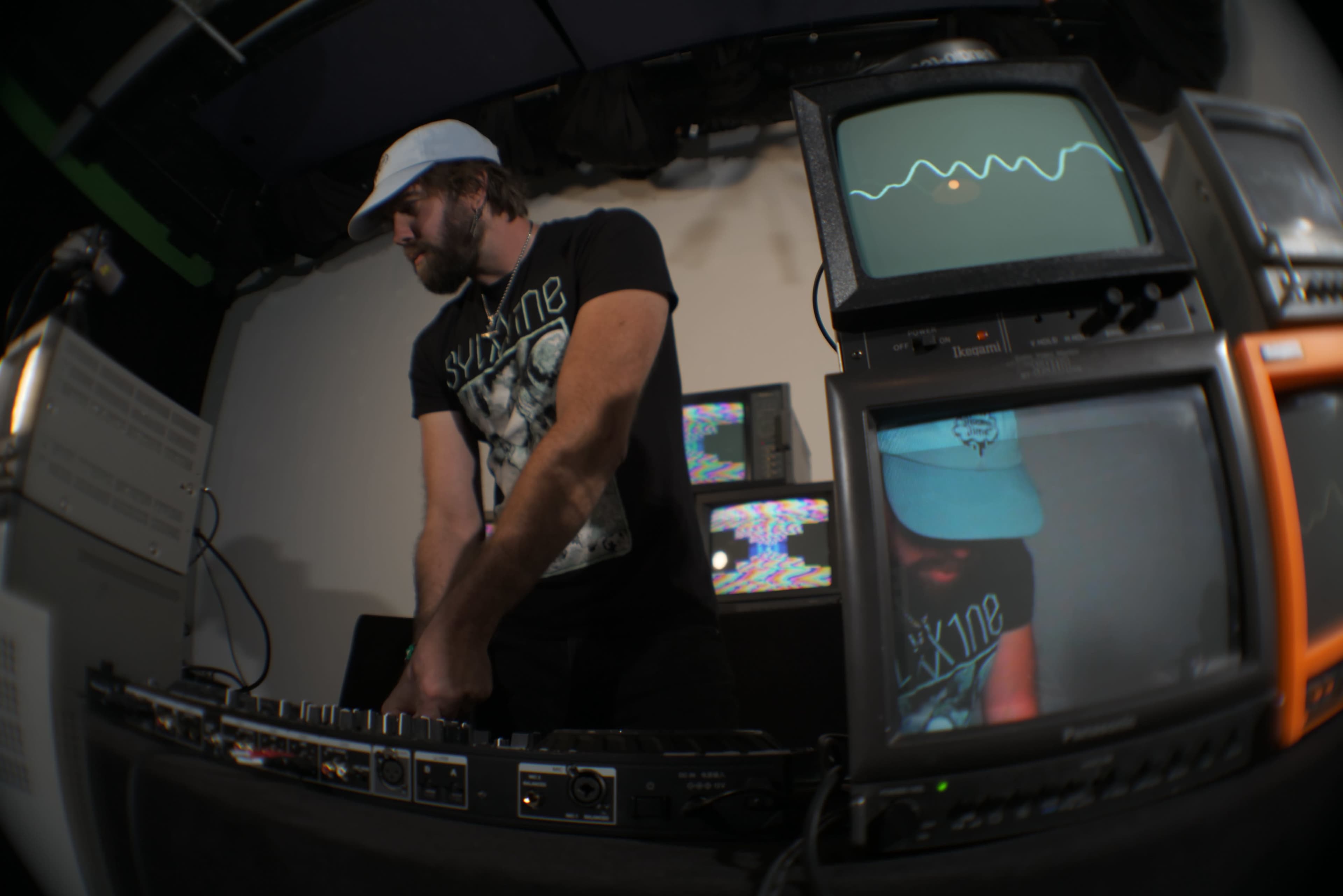 A DJ performs at a setup featuring multiple vintage monitors displaying abstract graphics.