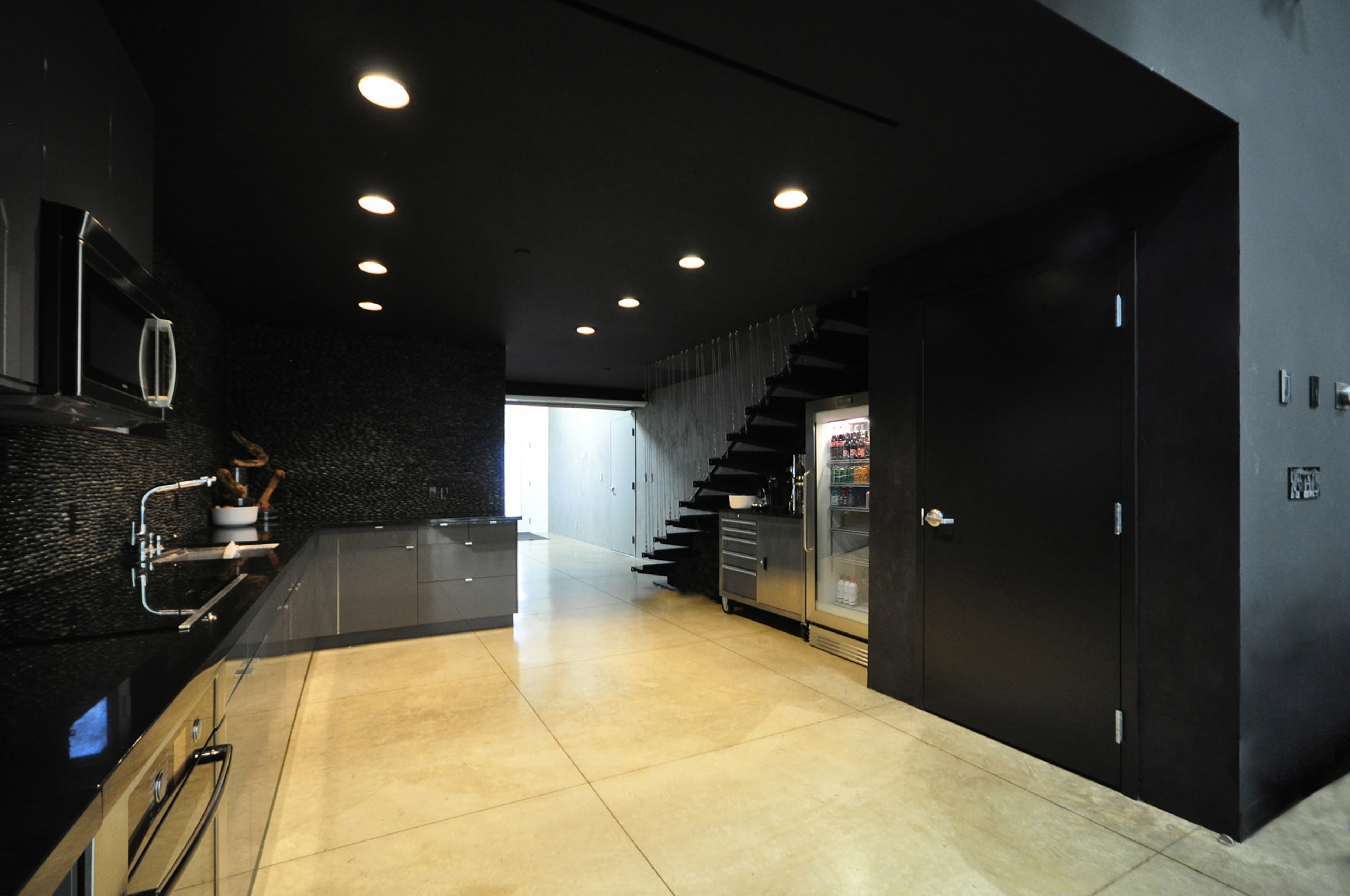 A modern kitchen with dark cabinetry, stainless steel appliances, and a staircase leading to an upper level.