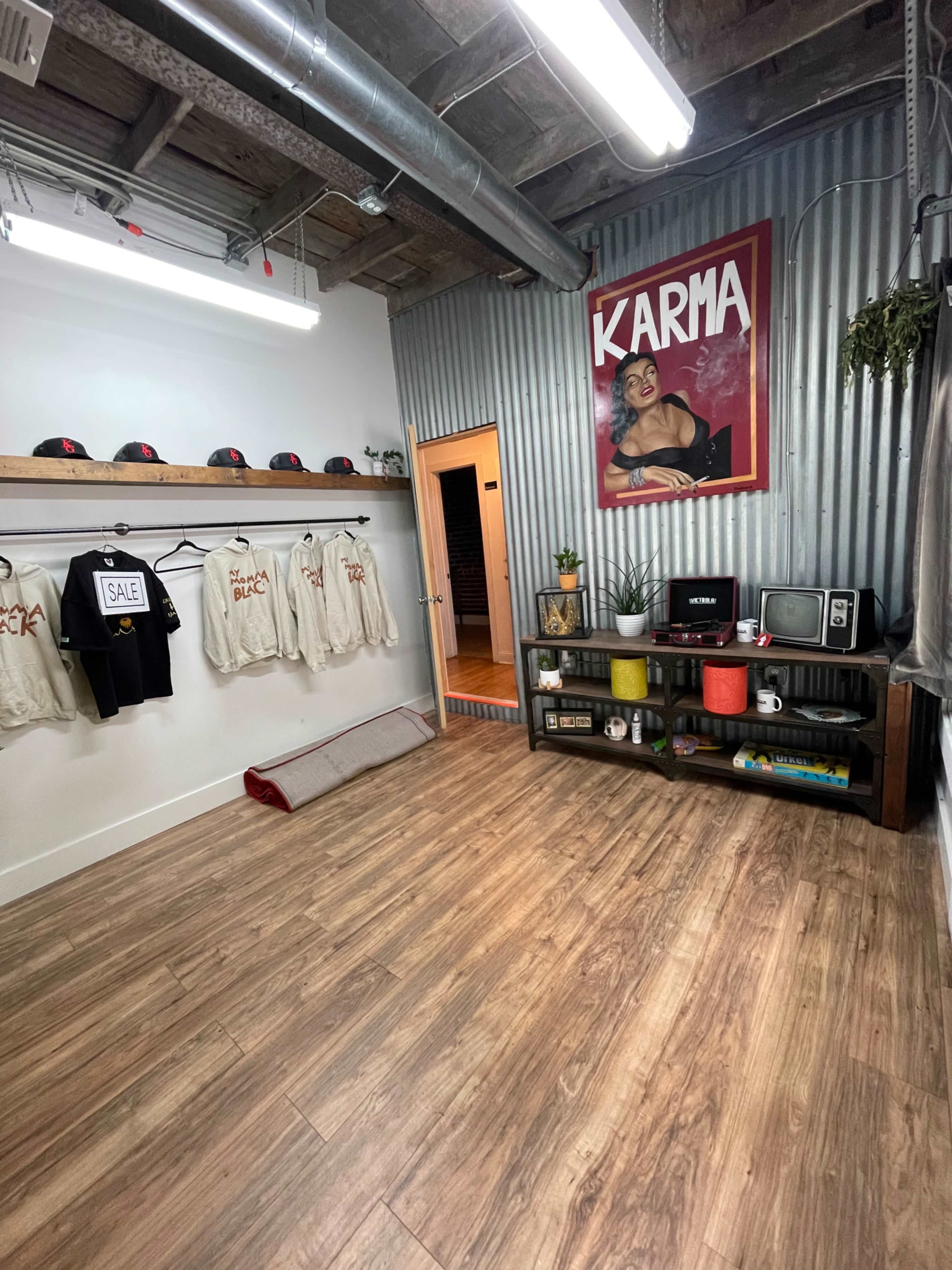 The image shows a stylish retail space with hanging sweatshirts, a shelving unit displaying various items, and a red poster on the wall that reads "KARMA."
