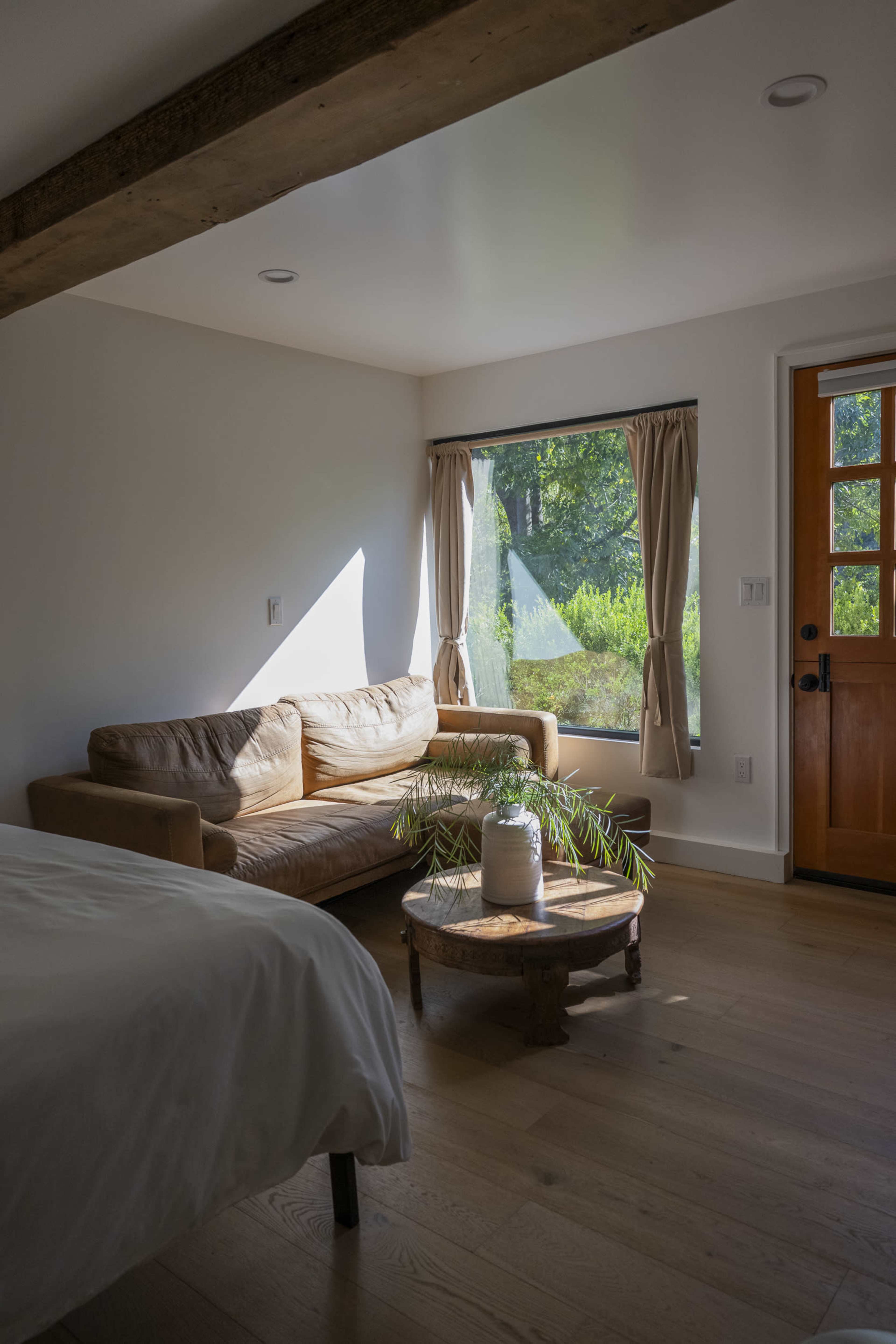 A cozy room features a brown couch and a wooden coffee table beside a large window with greenery visible outside.