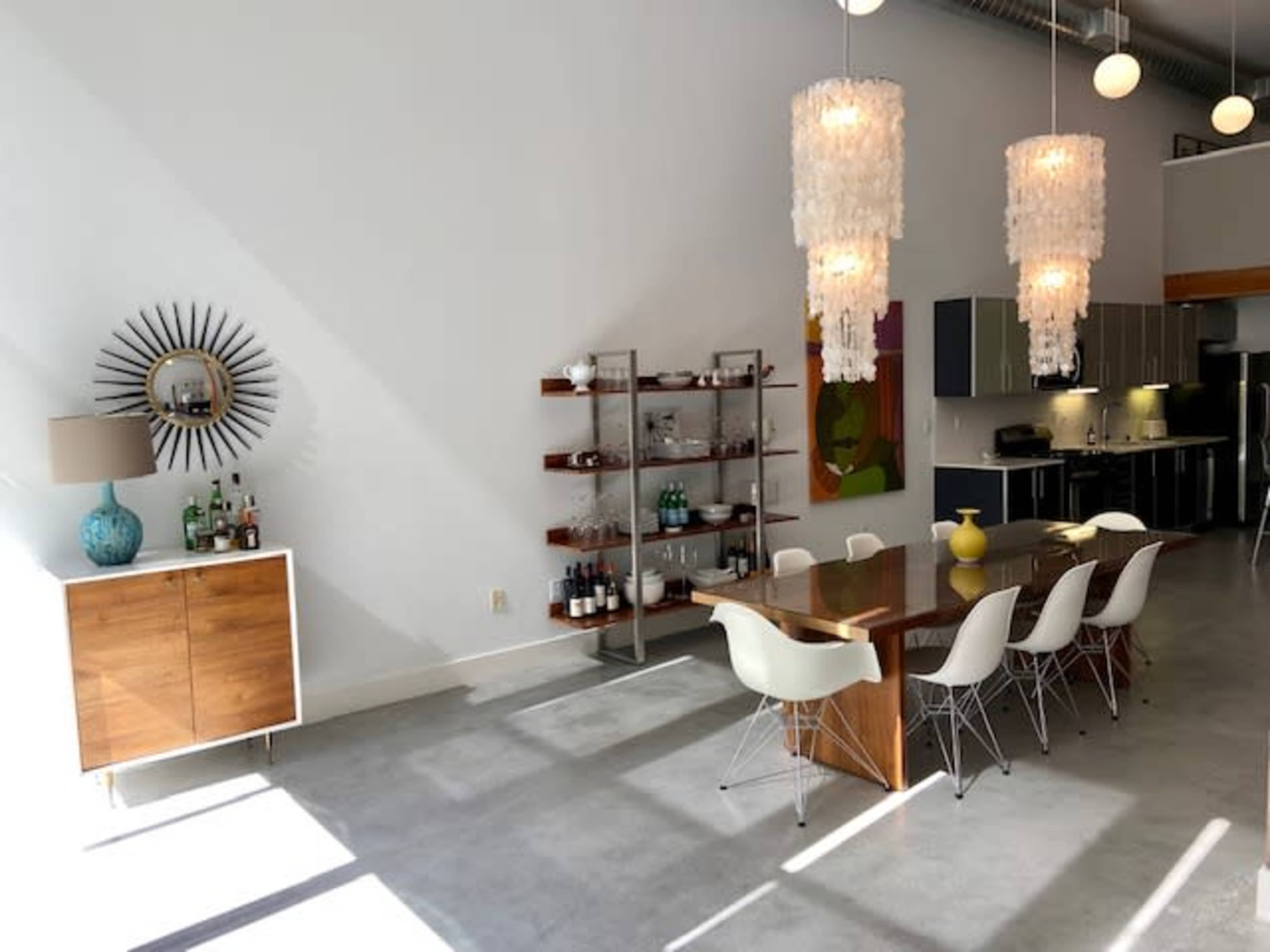 A modern dining area with a wooden table, white chairs, a sideboard, and two decorative light fixtures hanging from the ceiling.