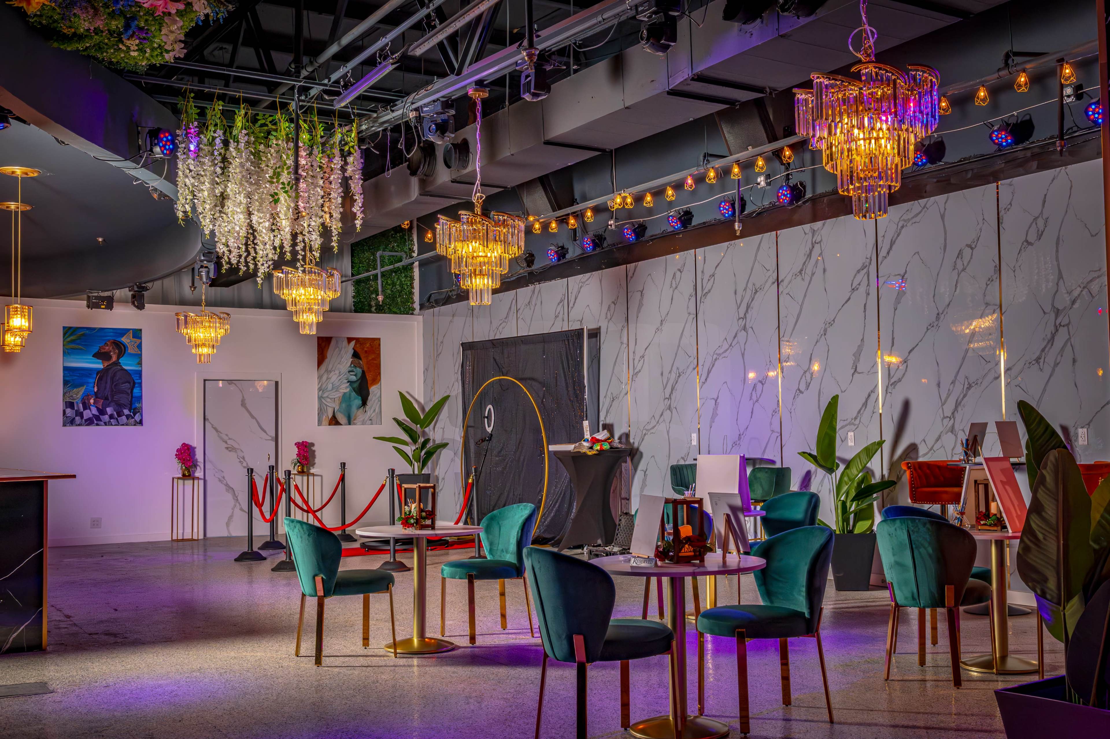 A modern event space features elegant chandeliers, marble walls, and stylish seating arrangements surrounded by decorative plants.