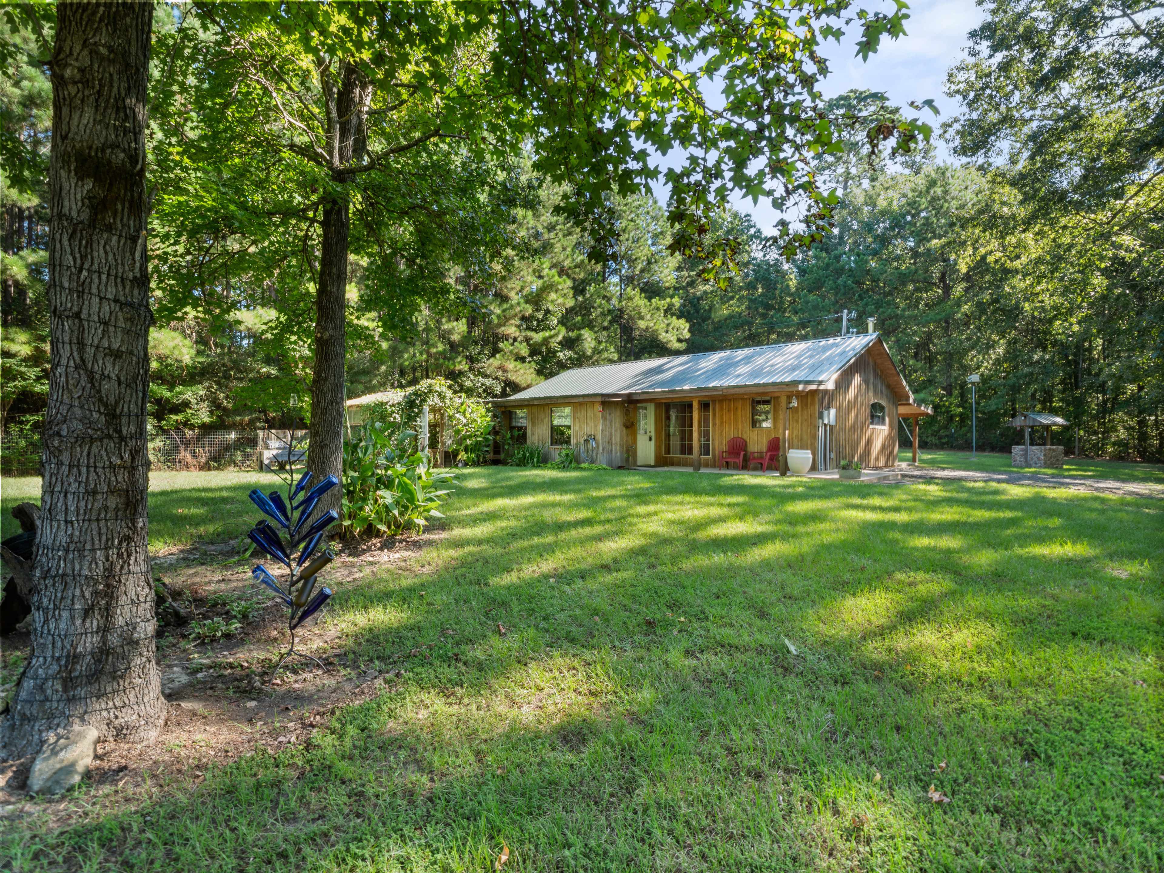 A wooden cabin with a metal roof is set in a grassy area surrounded by trees.