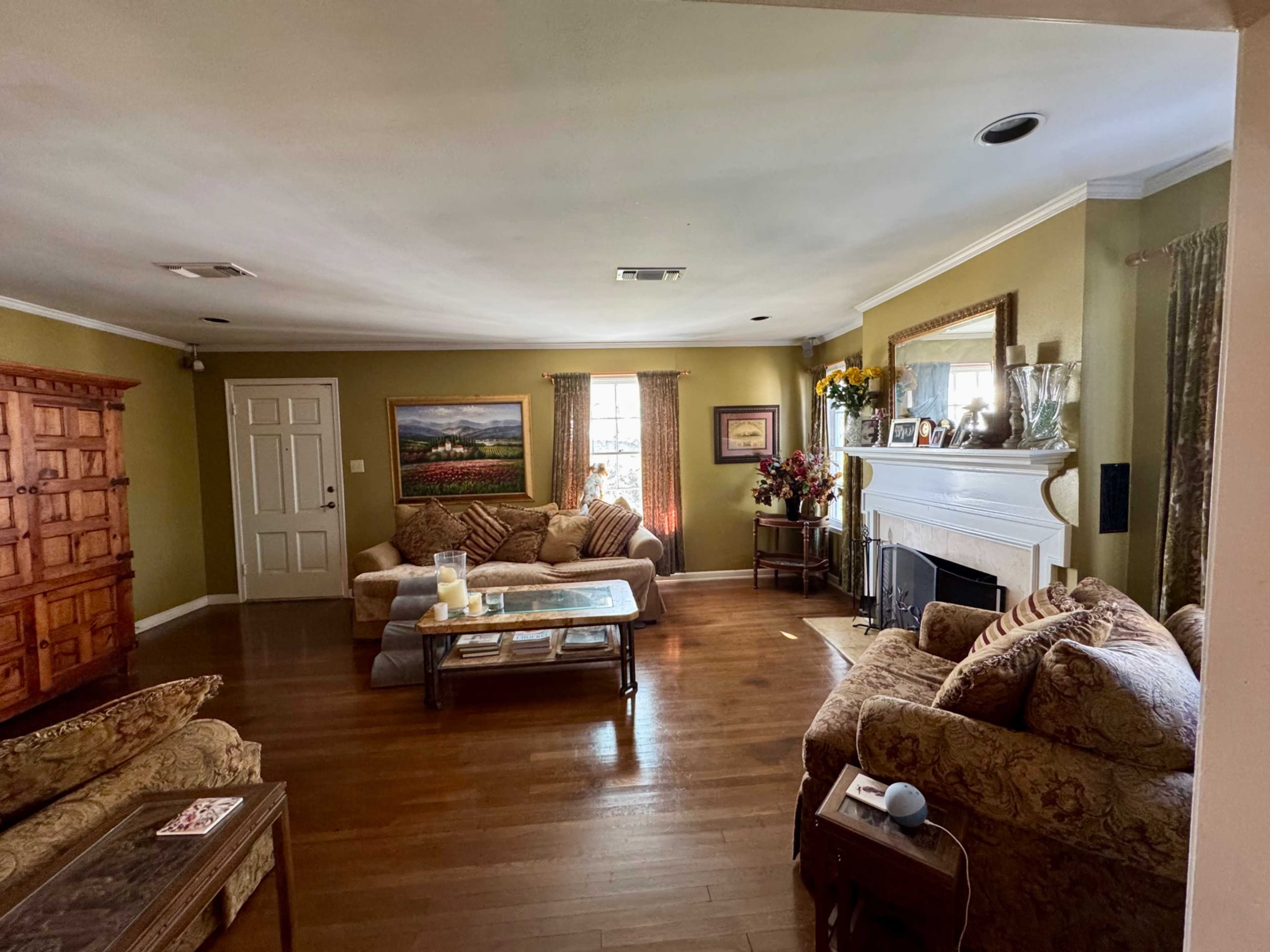 The image shows a well-furnished living room with a fireplace, two sofas, a coffee table, and a wooden cabinet against the wall.