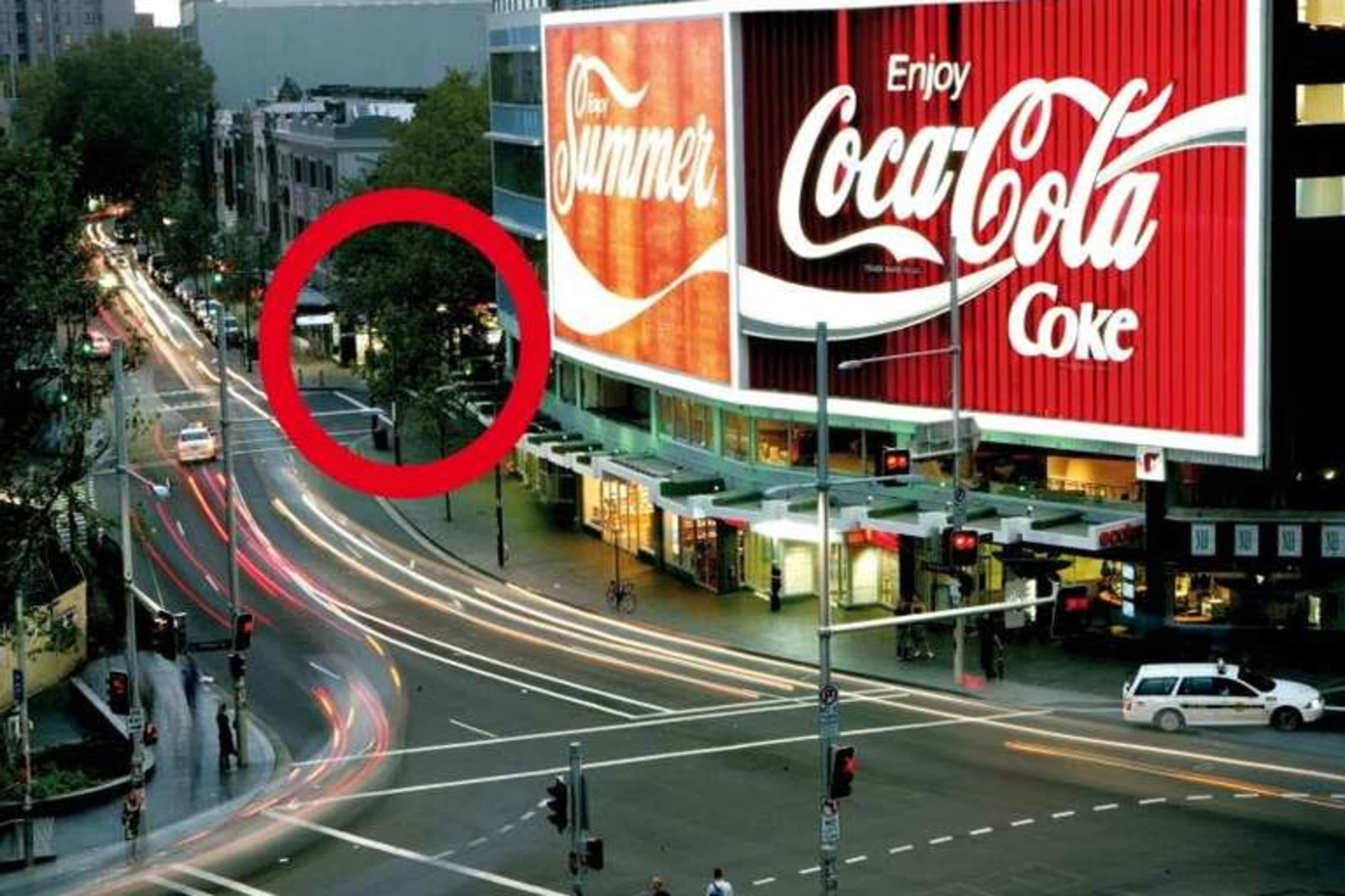 A large Coca-Cola advertisement is prominently displayed on a building near a busy intersection with traffic lights and moving vehicles.
