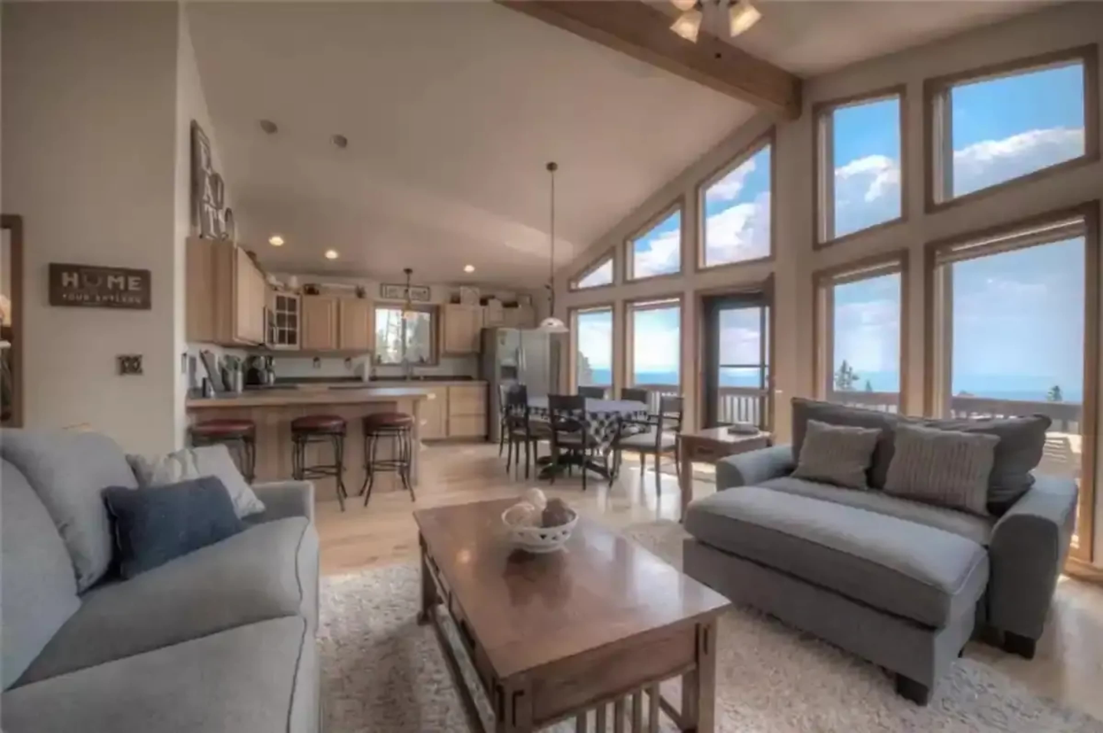 A modern living space with large windows, a kitchen area, and a dining table adjacent to a comfortable seating arrangement.