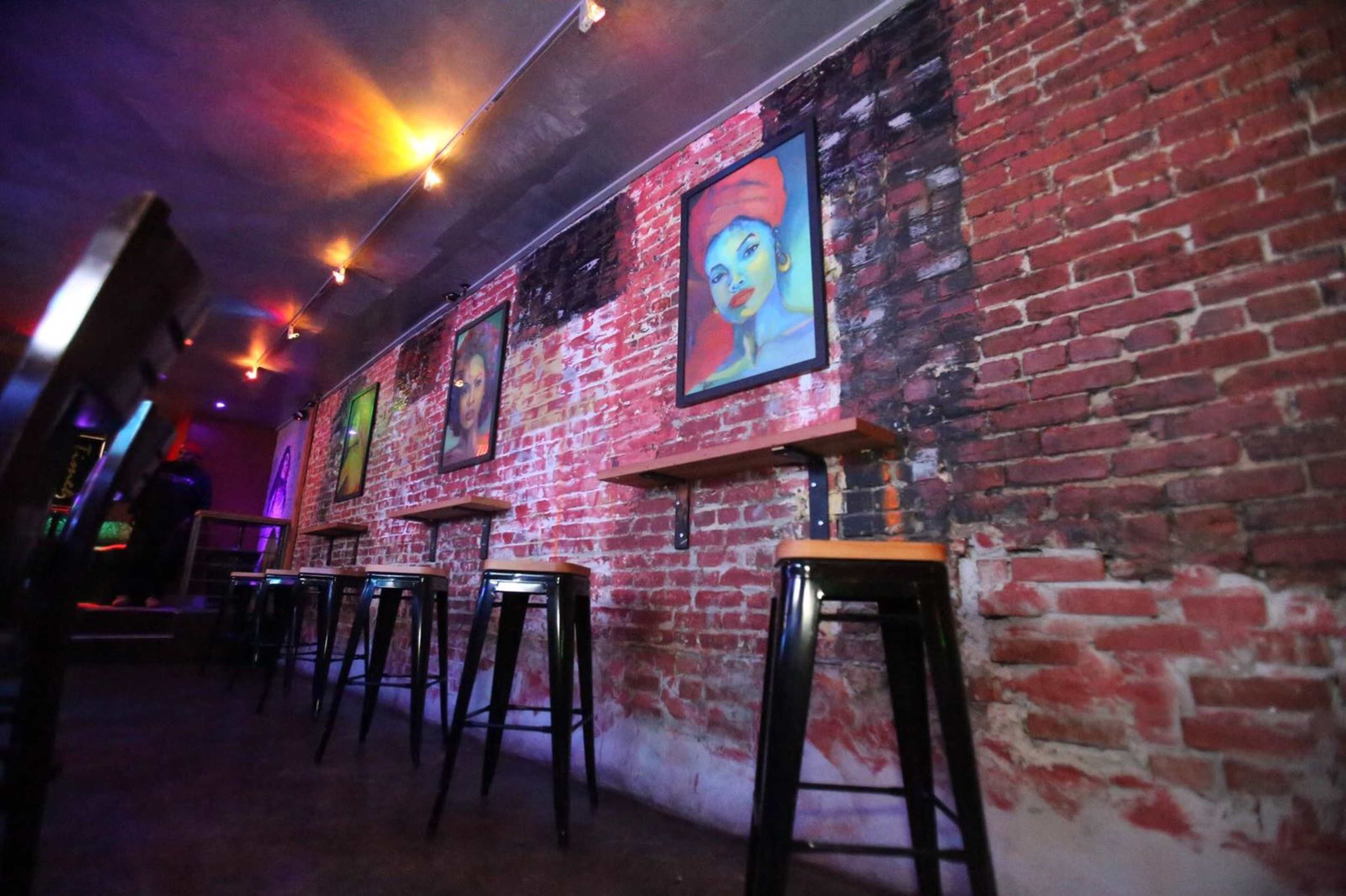 A dimly lit bar area with exposed brick walls and several framed portraits hanging on the wall.