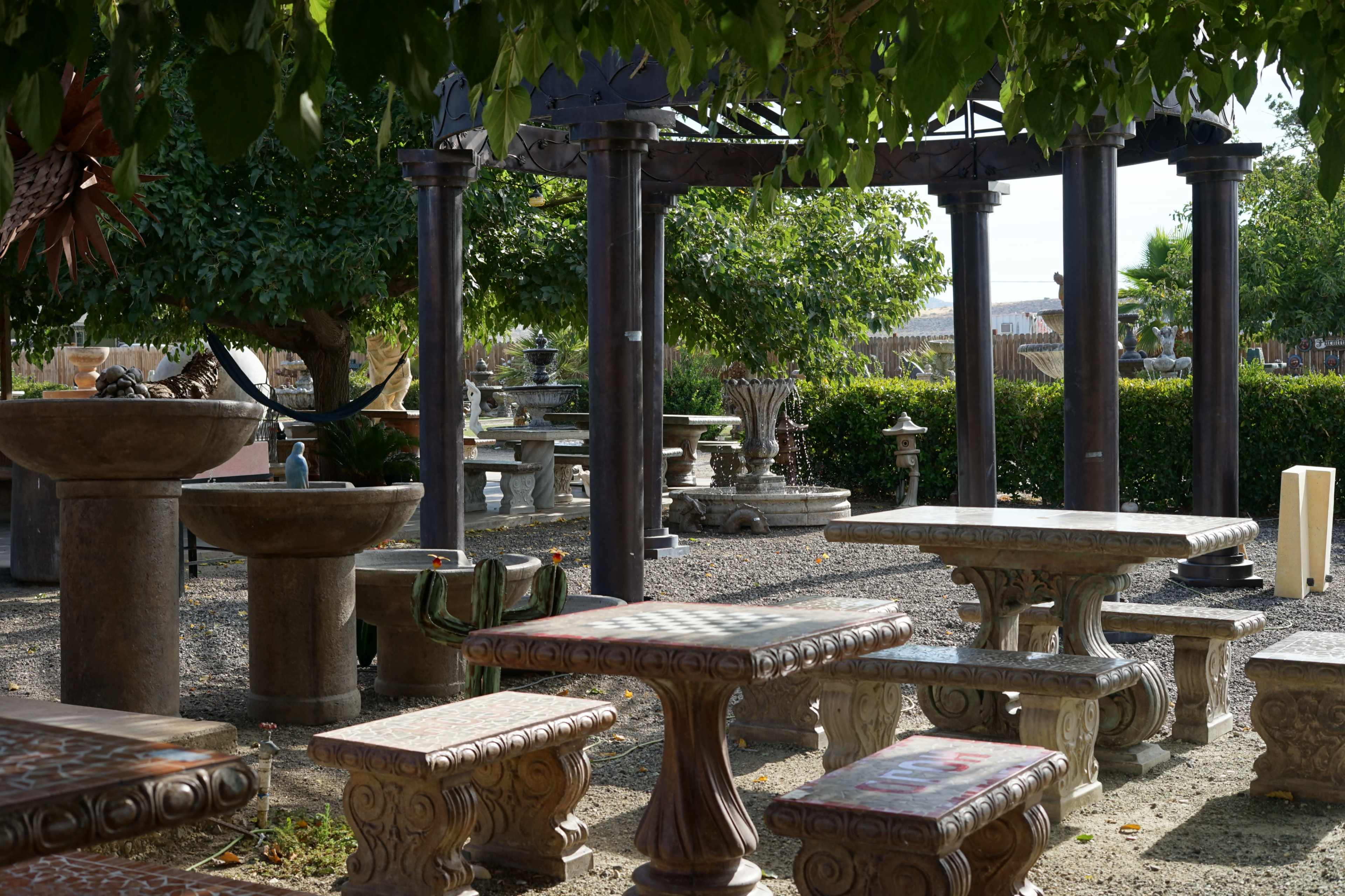 The image shows a landscaped outdoor area with stone tables and decorative fountains under a shaded structure.