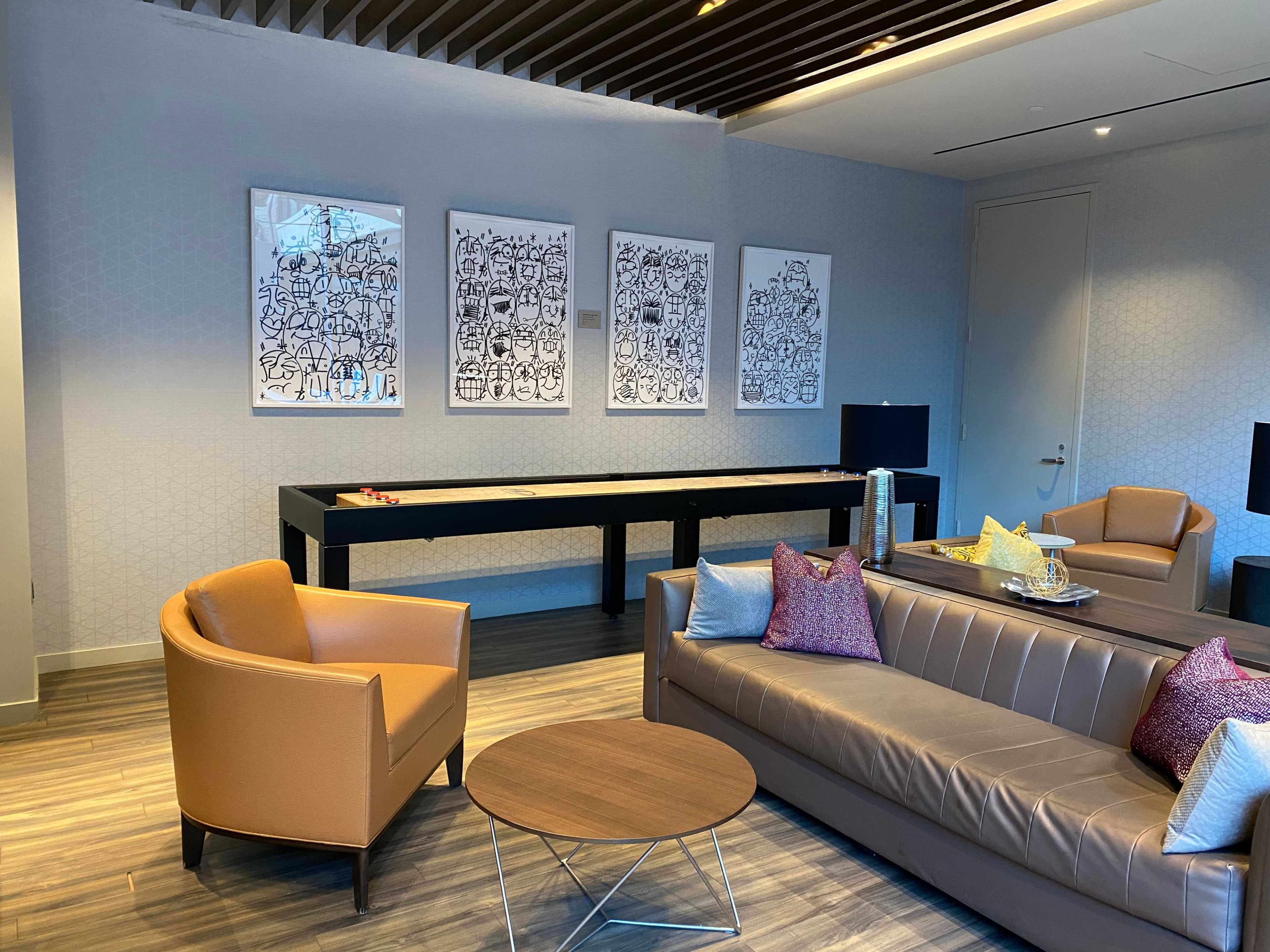 A modern lounge area featuring a sofa, two armchairs, a round coffee table, and three art pieces on the wall.