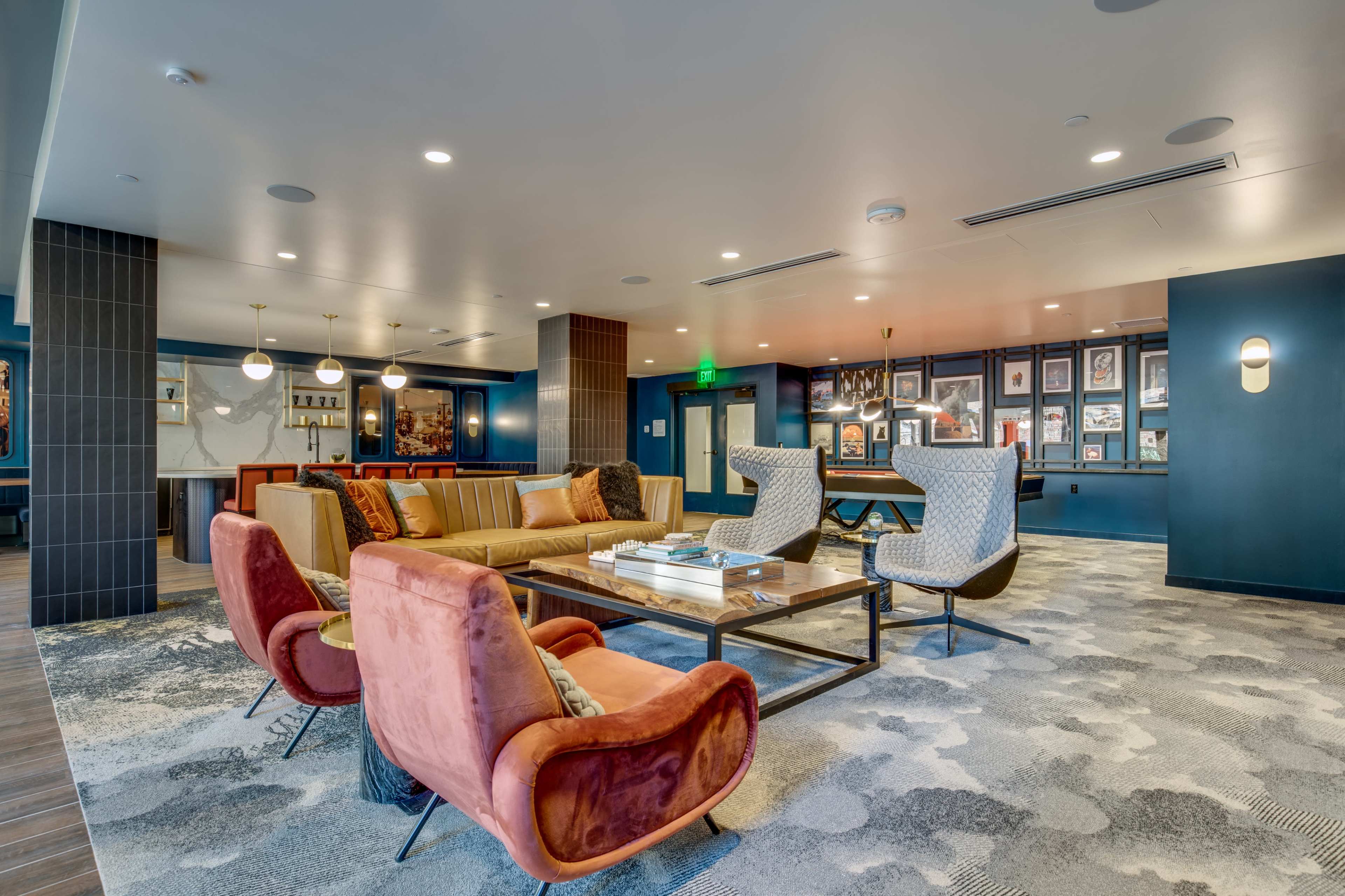 A modern lounge area featuring a seating arrangement with colorful armchairs and a sofa, a coffee table, and framed artwork on the walls.