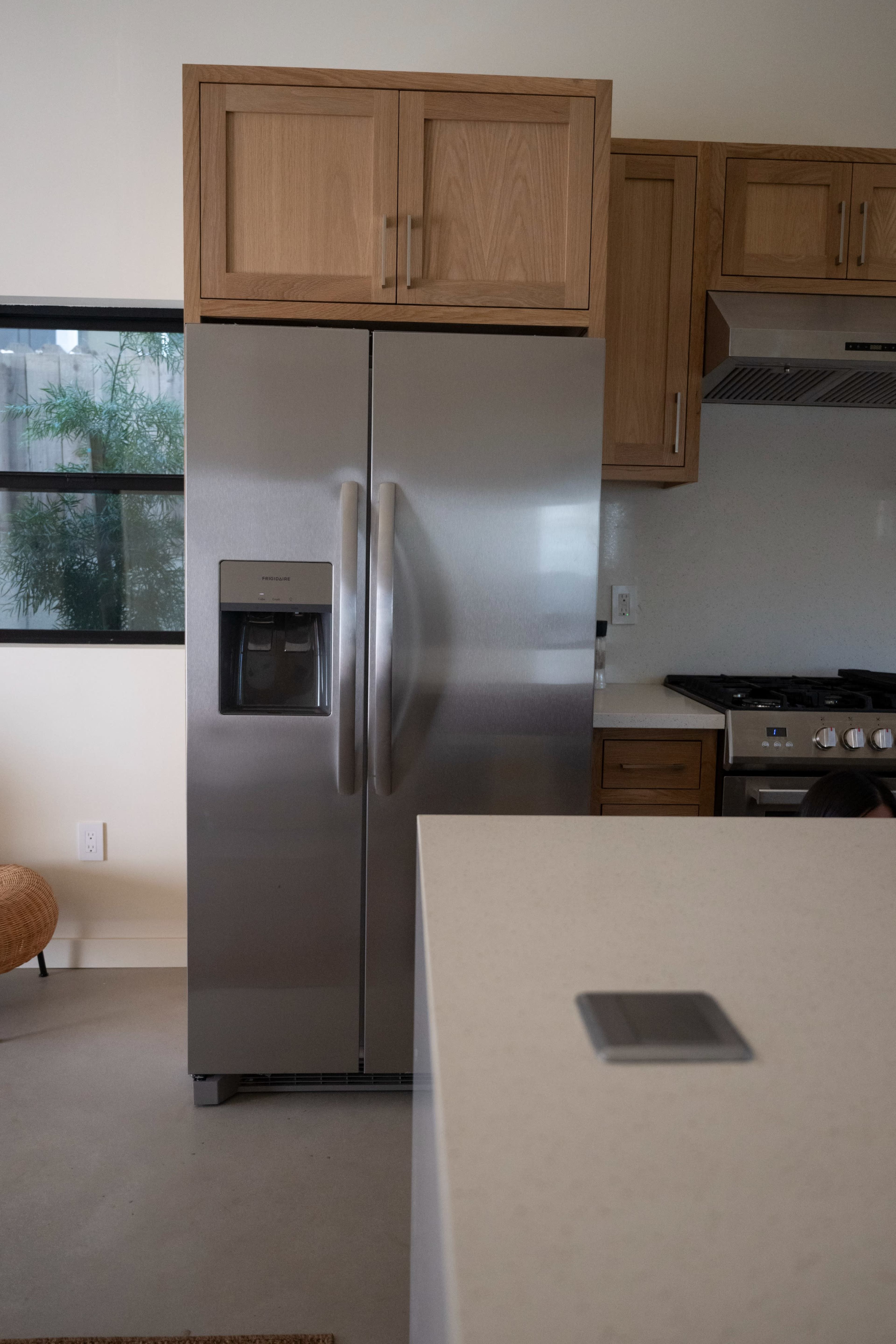 The image shows a stainless steel refrigerator next to wooden cabinets in a modern kitchen with a countertop.