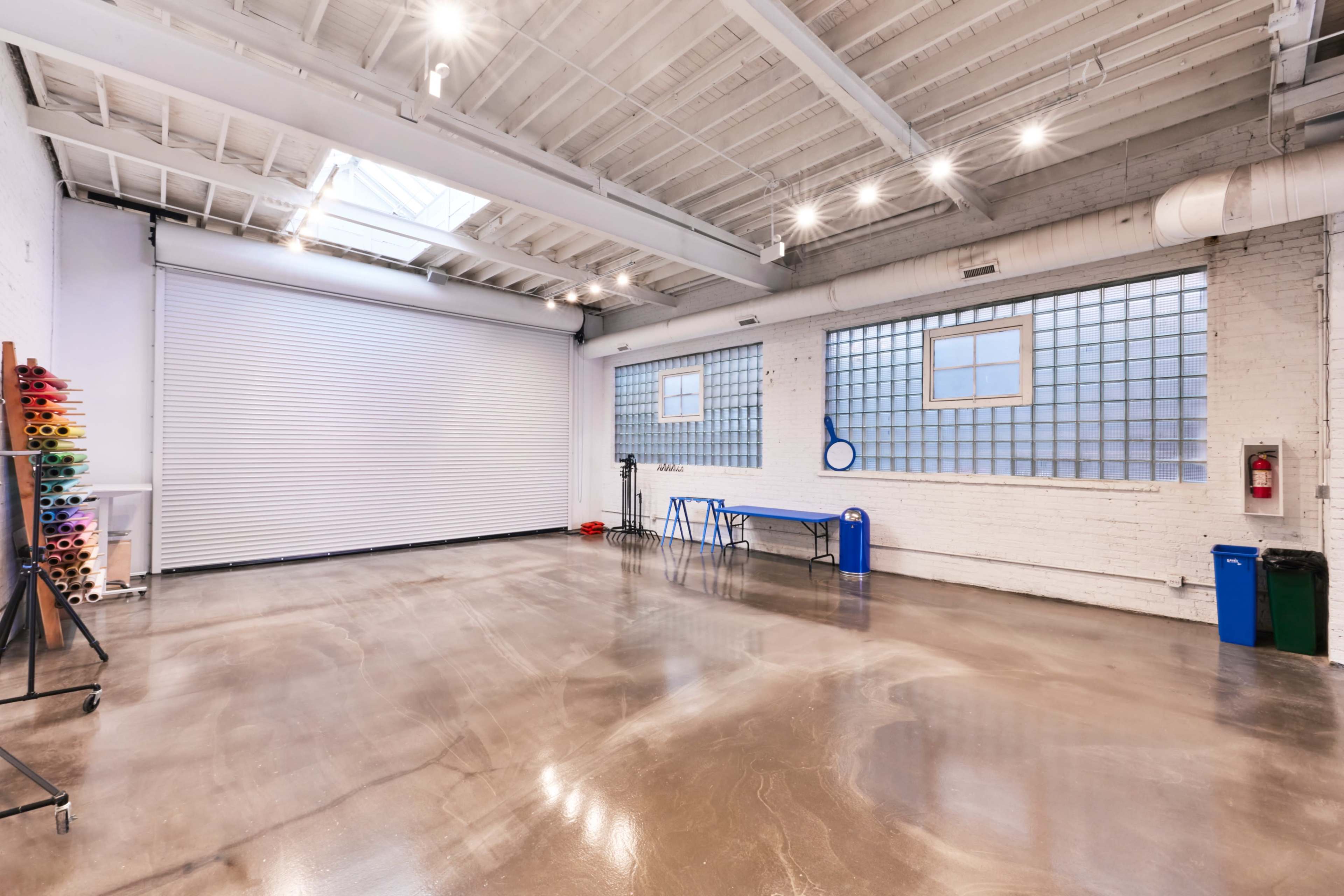 A spacious, well-lit industrial room with concrete floors, large windows, and a roll-up garage door.
