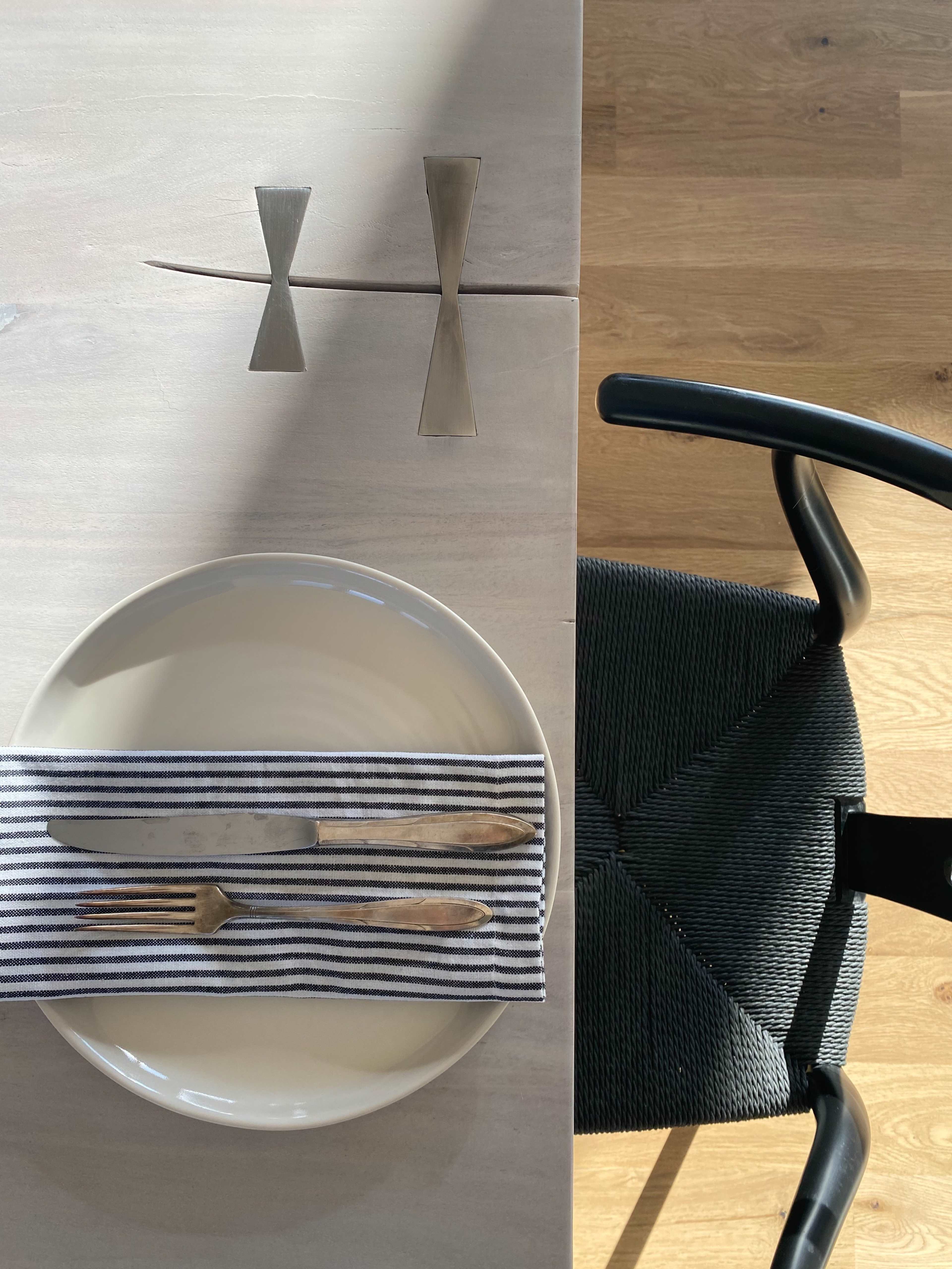 A neatly arranged dining table features a plate on a striped napkin, accompanied by a knife and fork, with modern silverware placed above.