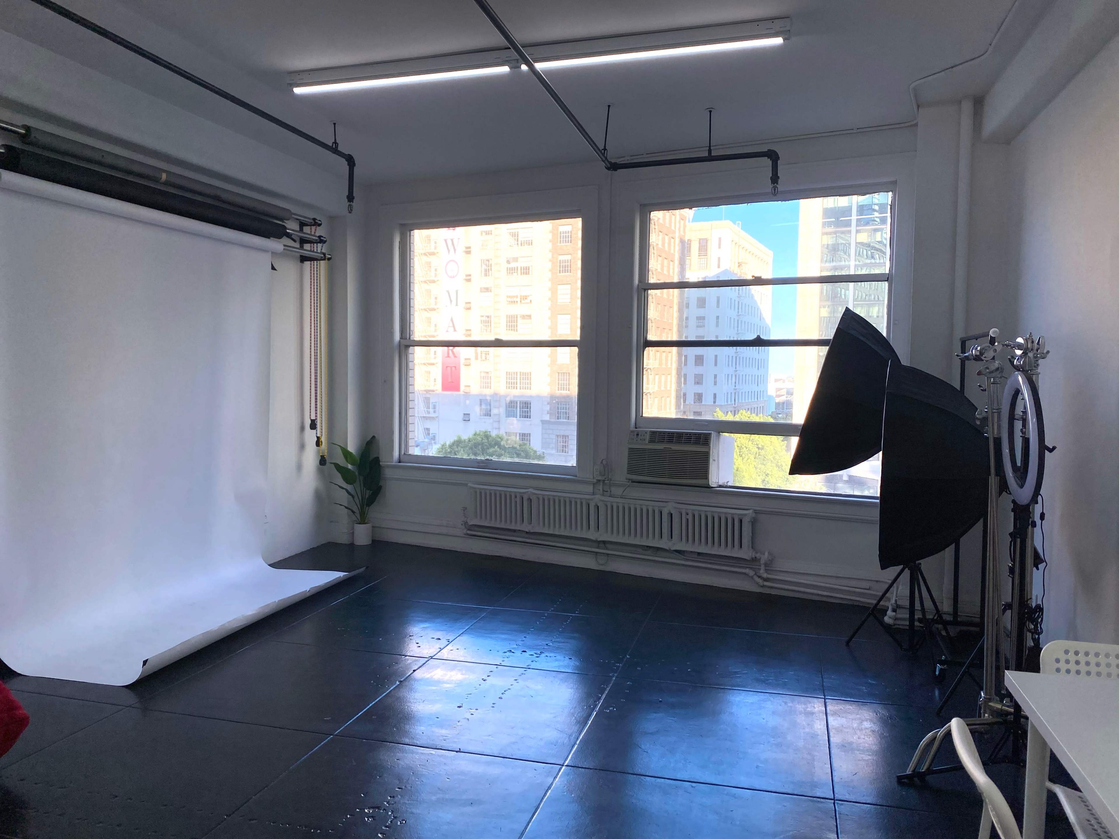 A photography studio with a white backdrop, large windows, and studio lighting equipment in the corner.