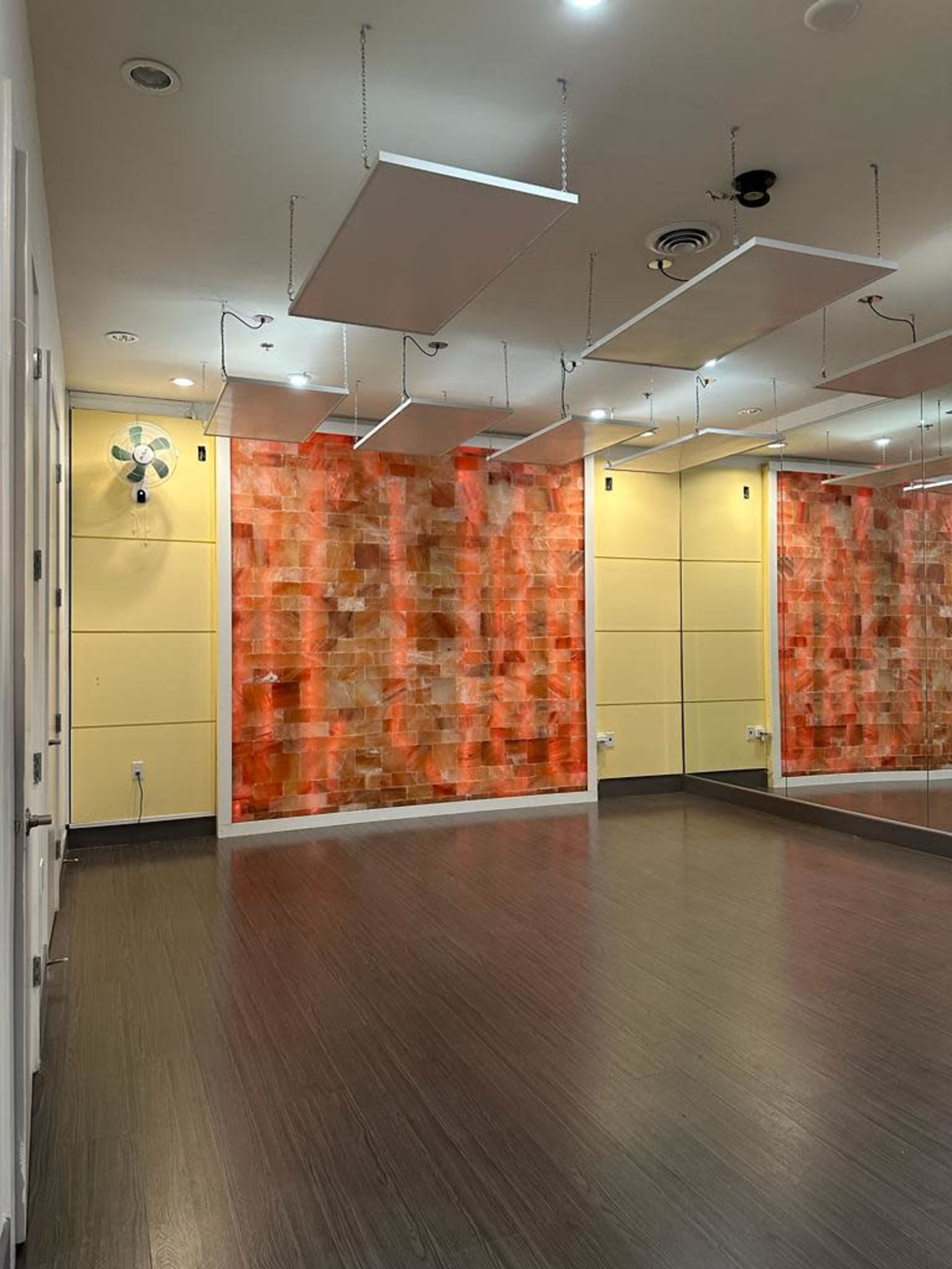 A dance studio featuring a wooden floor, brightly colored abstract wall art, mirrors on one side, and suspended ceiling panels.