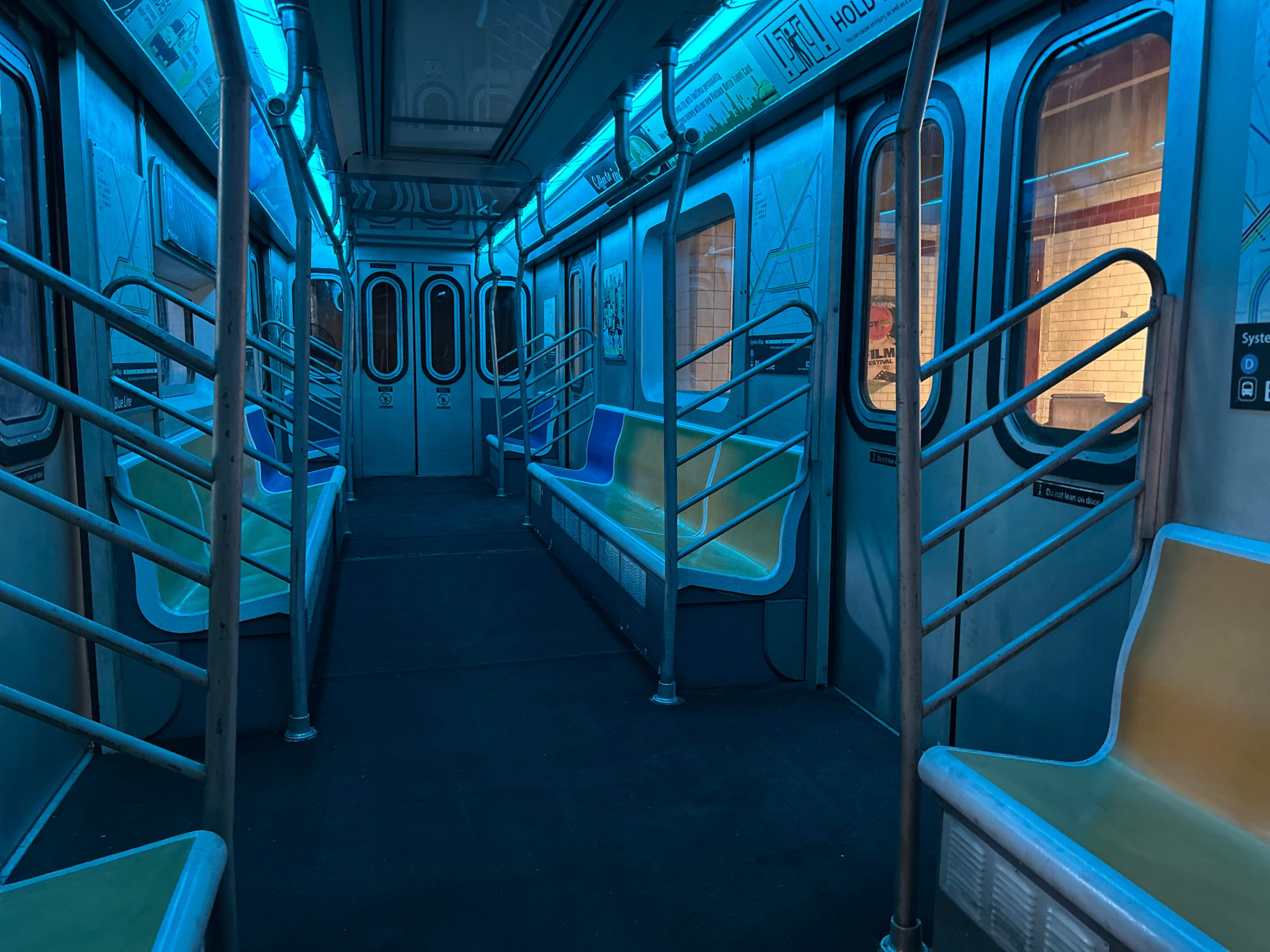 An empty subway car with blue lighting and colorful seating is visible.