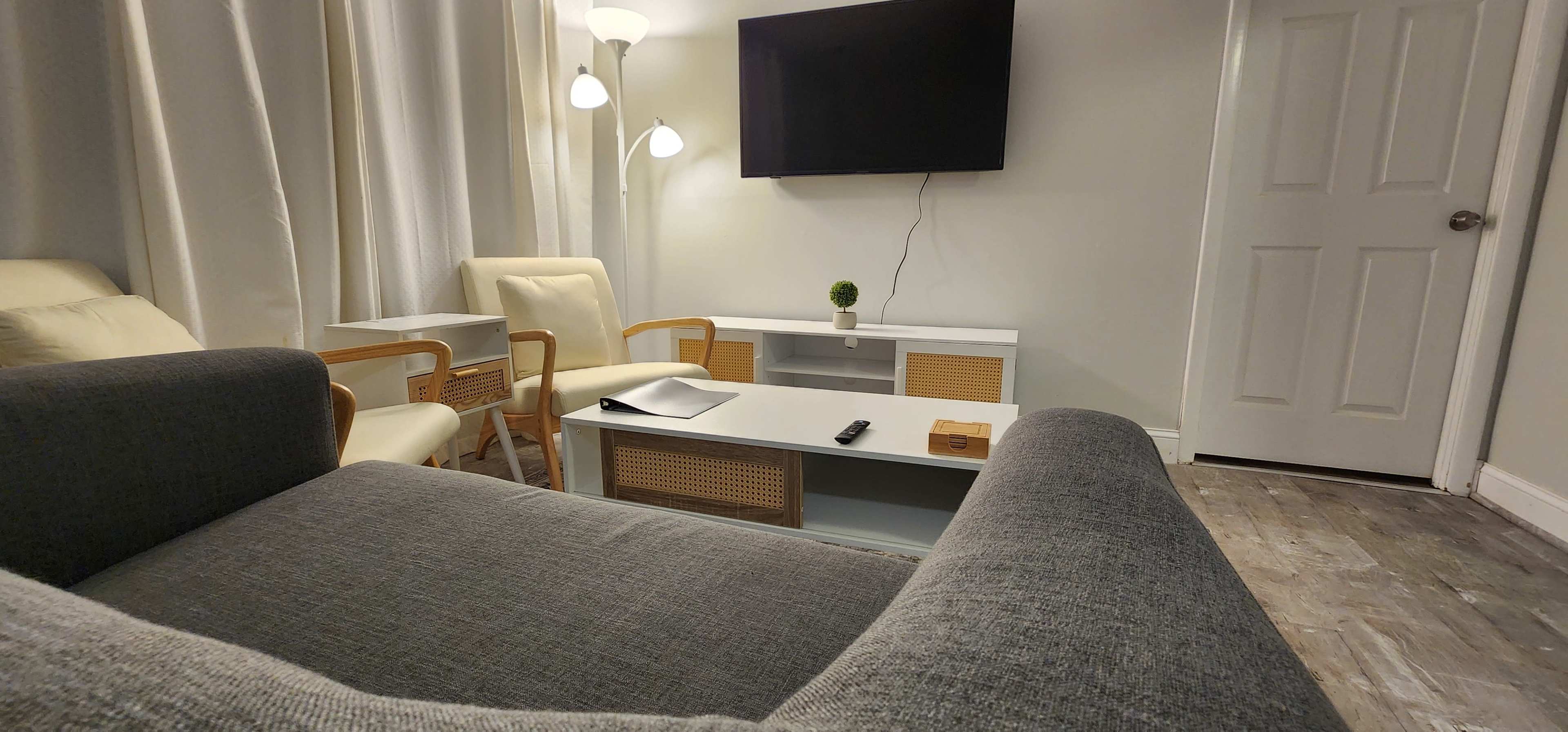 A modern living room features a couch, a coffee table, two chairs, a flat-screen TV, and a closed door.