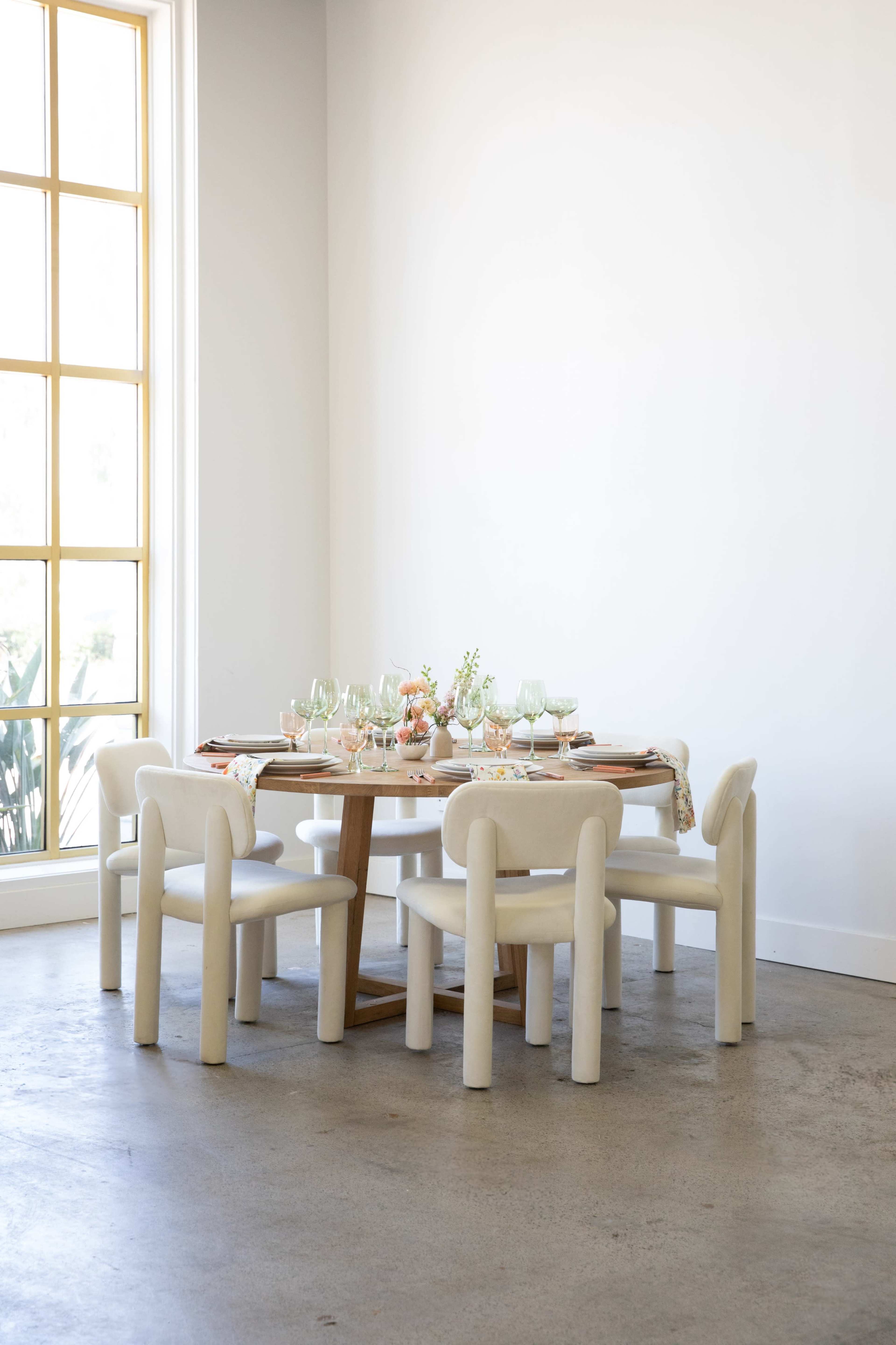 A dining table set for a meal is positioned in a brightly lit room with large windows.