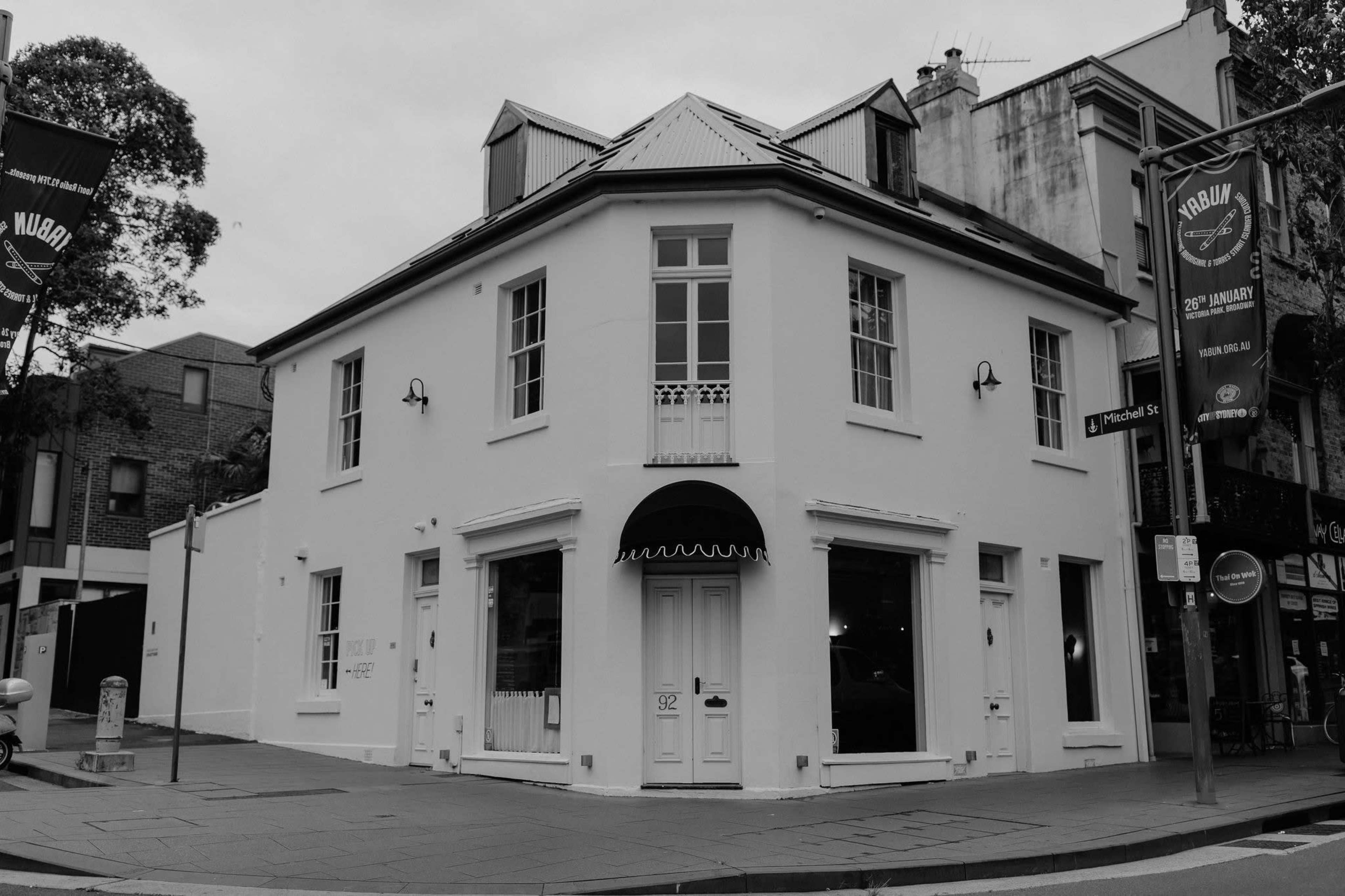 A white, two-story building with large windows, located on a street corner, featuring a black awning above the entrance.