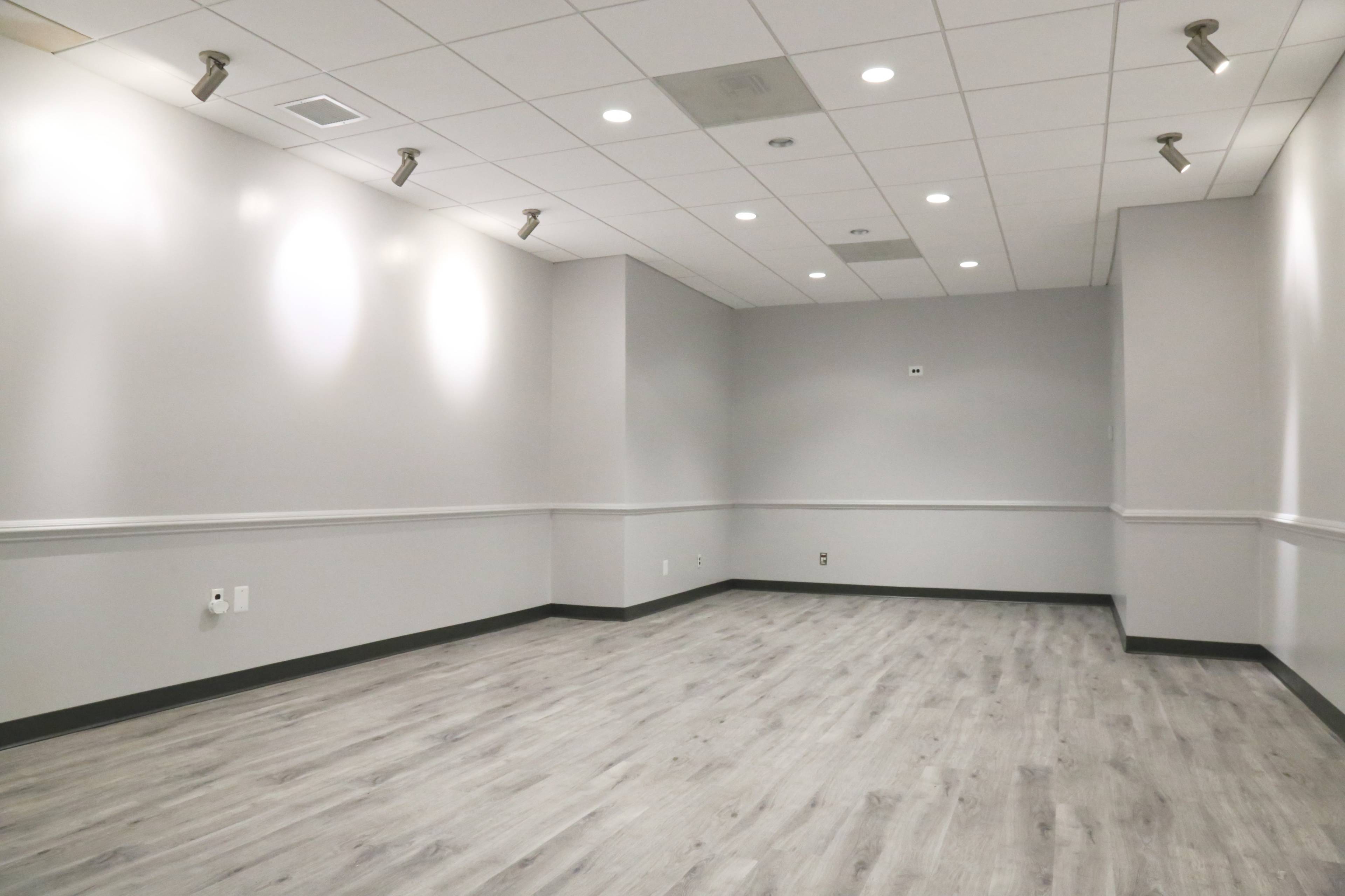 A well-lit, empty room featuring gray walls, a wood-like floor, and a simple ceiling design.