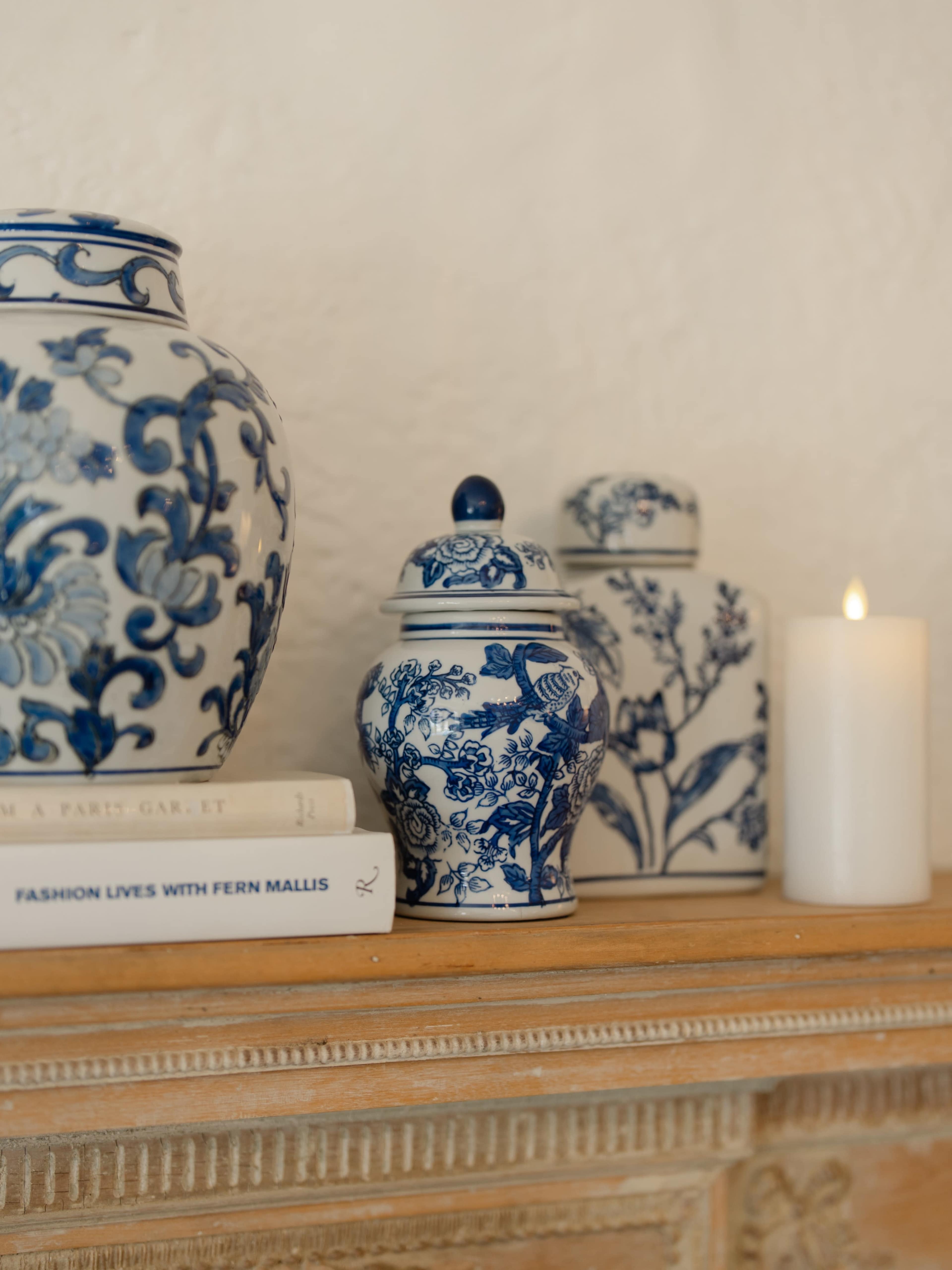 The image shows a collection of blue and white decorative porcelain jars alongside a candle and books on a wooden mantel.