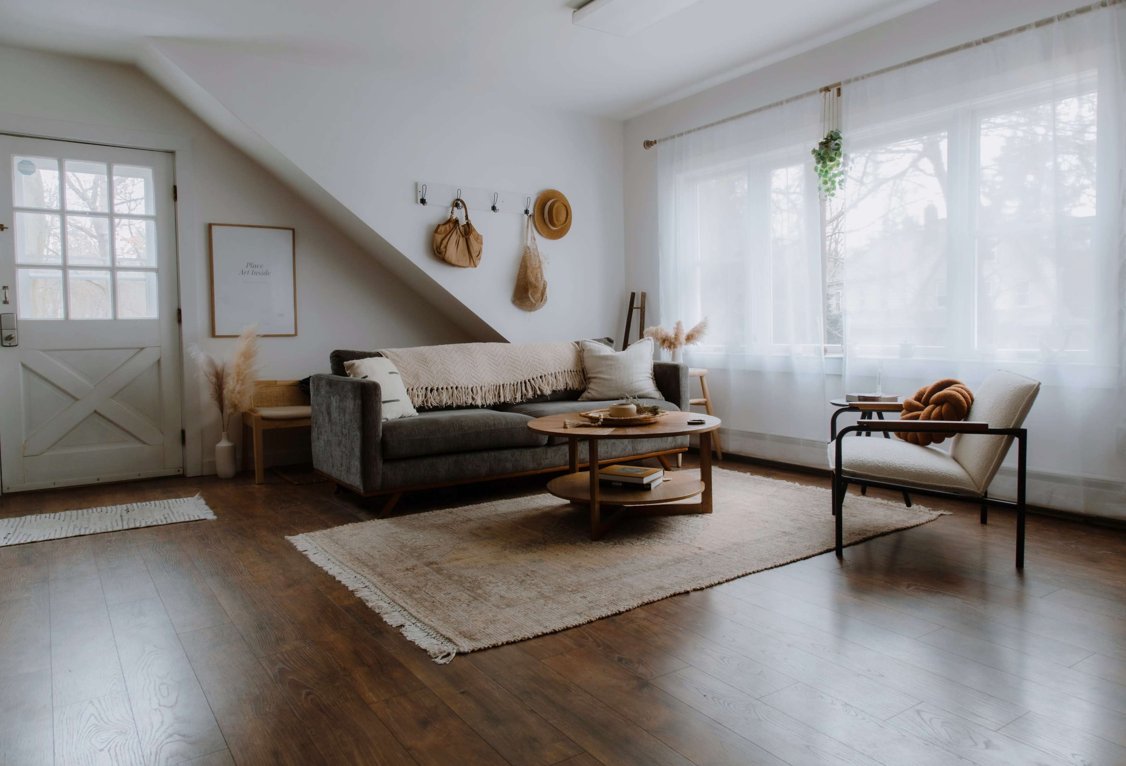 A minimalist living room features a gray sofa, a round coffee table, and a large window with sheer curtains, all set against wooden flooring.