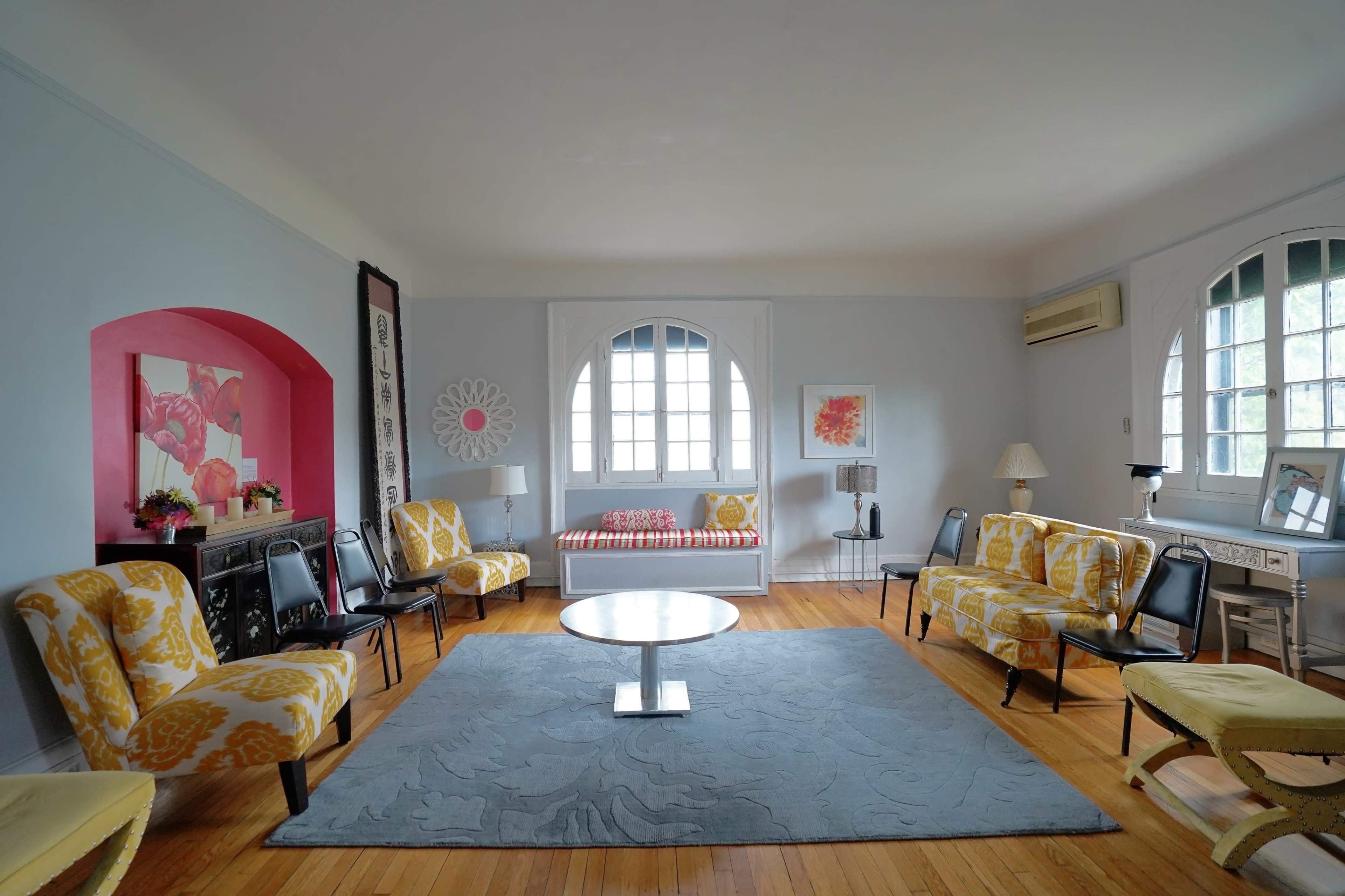 A spacious living room features yellow upholstered chairs, a circular coffee table, and large windows with a view of the outdoors.
