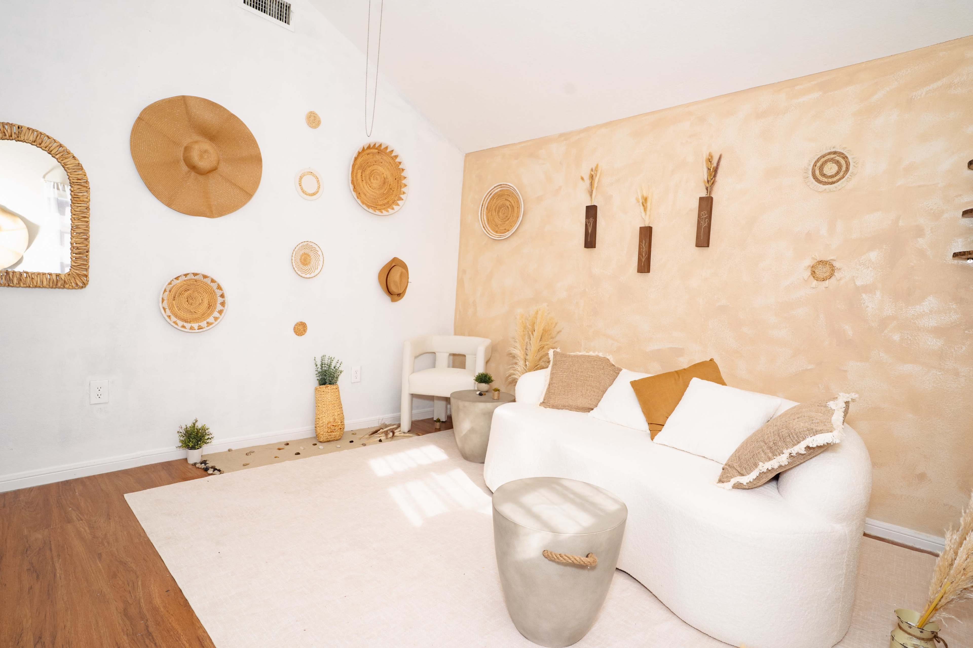 The image depicts a modern living room with a white curved sofa, a beige area rug, and decorative wall art made of natural materials, creating a warm, inviting atmosphere.