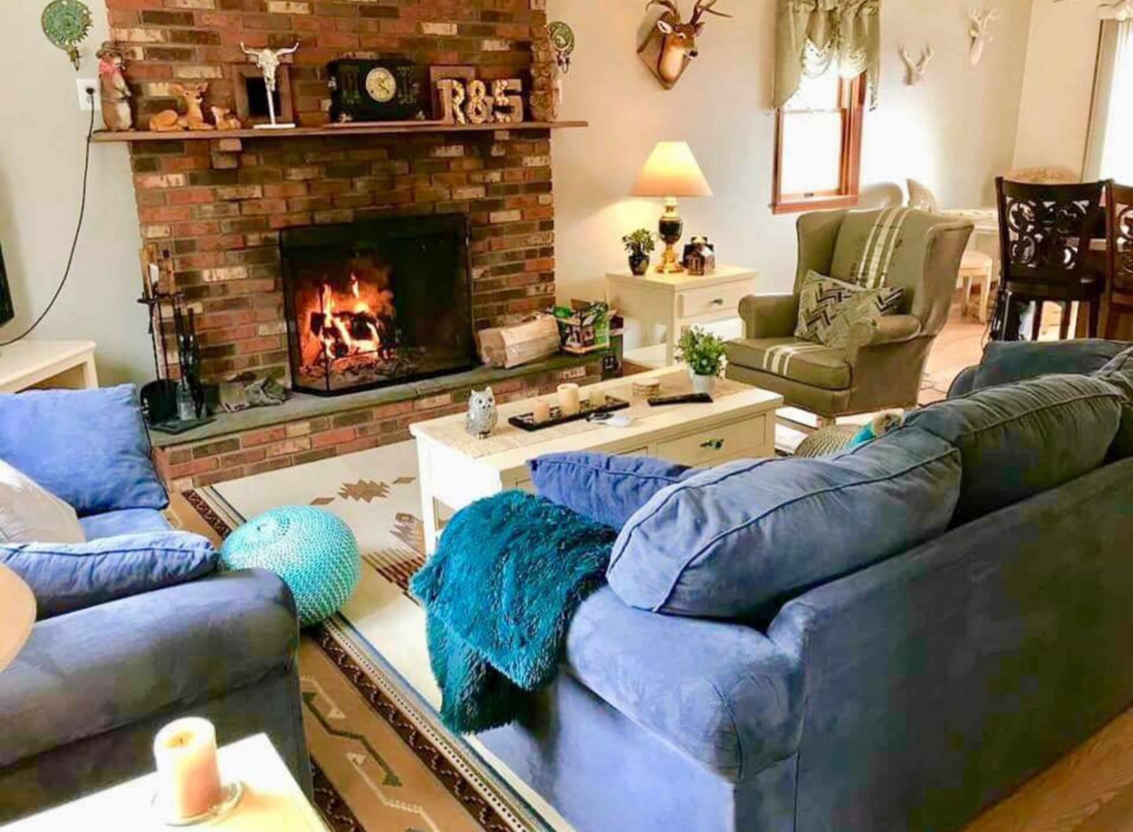 A cozy living room with two blue sofas facing a brick fireplace, which is aglow with a fire, and various decorative items arranged on a coffee table.