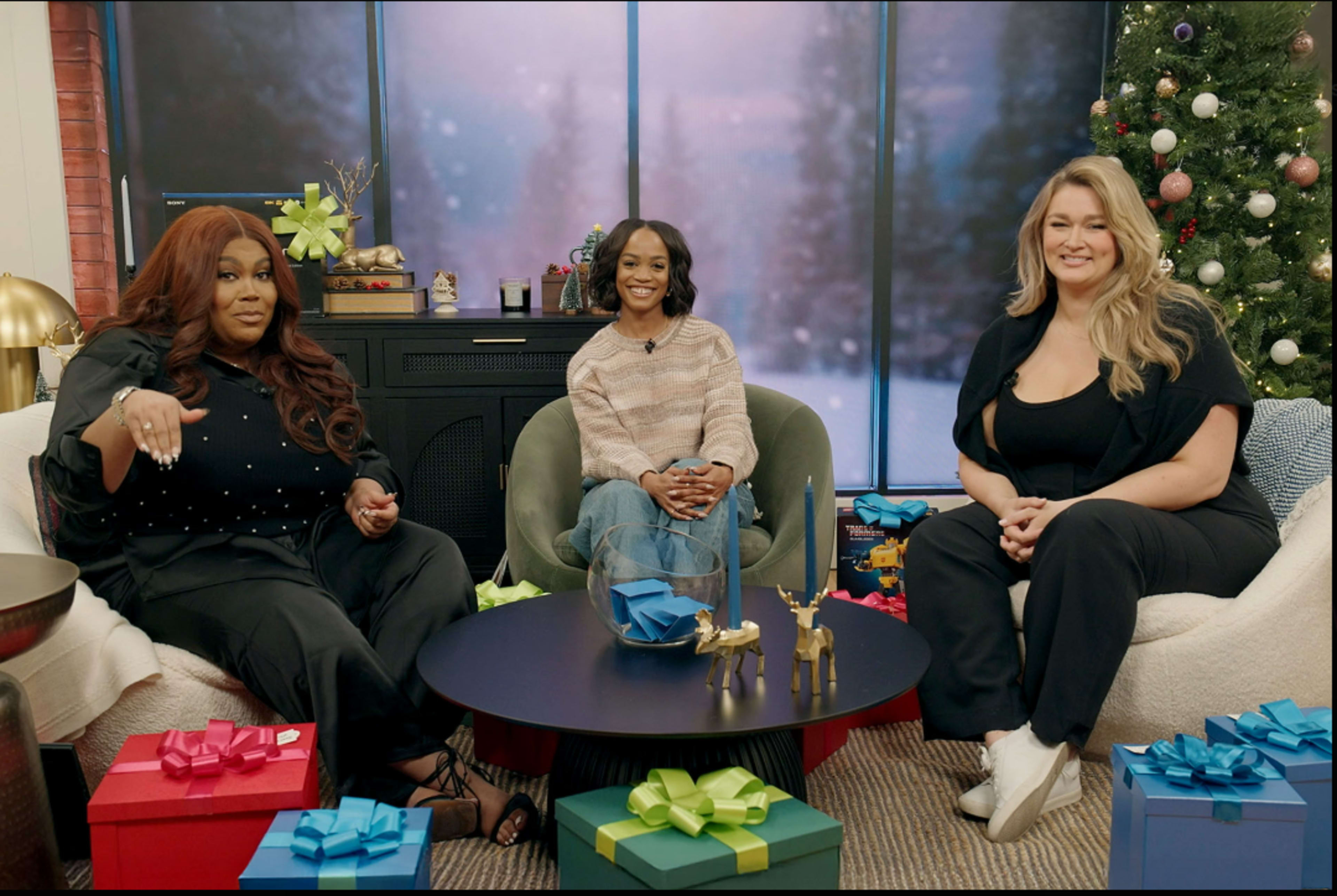 Three women are sitting on a couch in a cozy indoor setting, surrounded by holiday decorations and wrapped gifts.