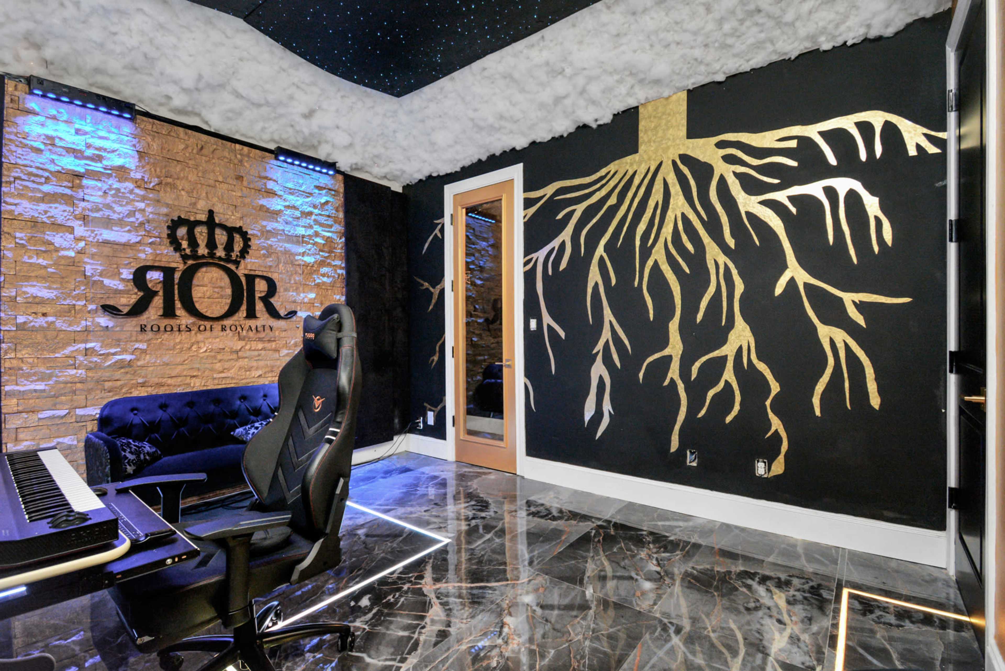 The image shows a modern room with a black wall featuring a gold tree root design, a mirrored door, and a dark-colored couch beside a keyboard setup on a marble floor.