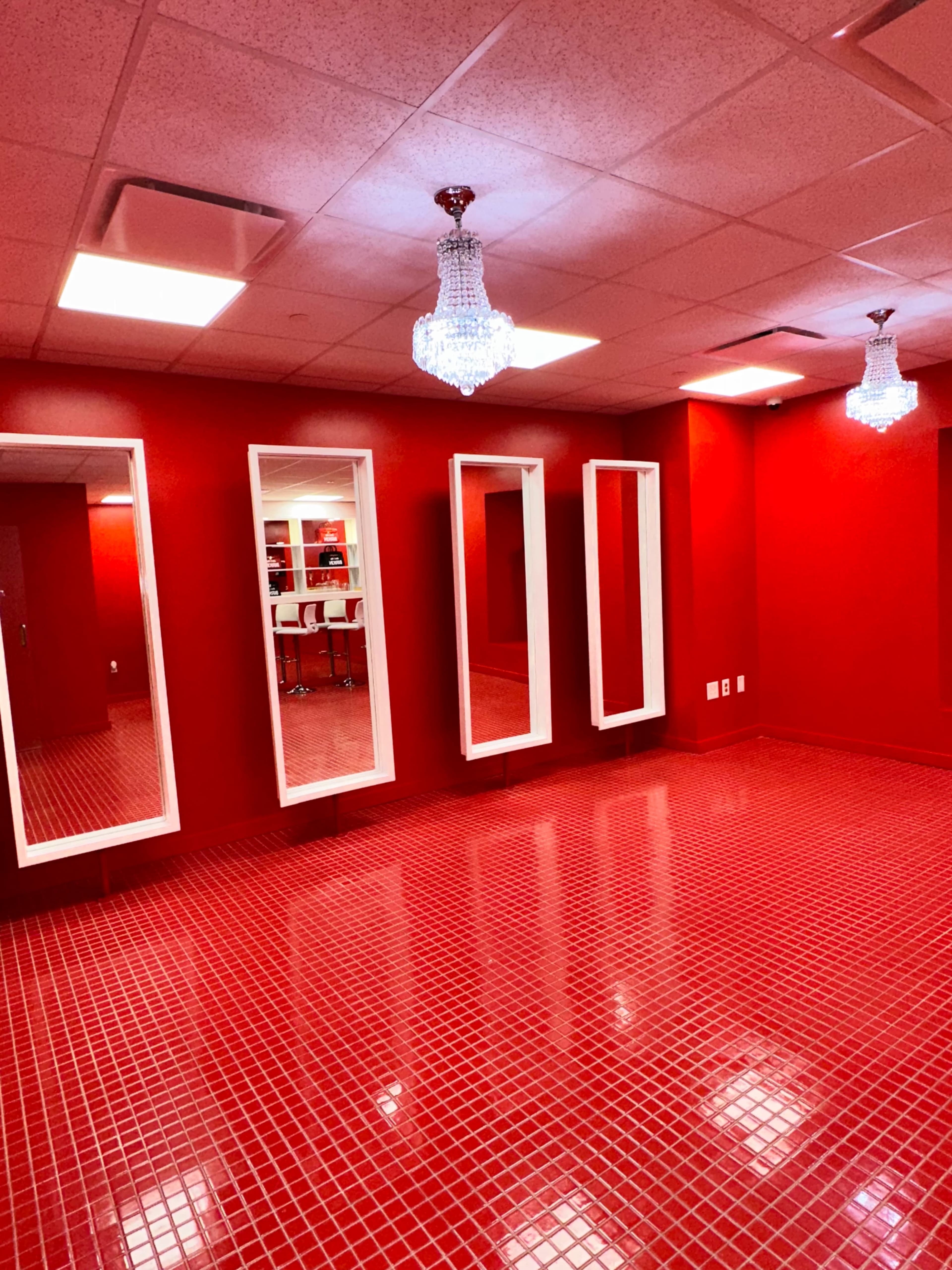The room features bright red walls, a tiled floor, and three large mirrors, illuminated by two crystal chandeliers.
