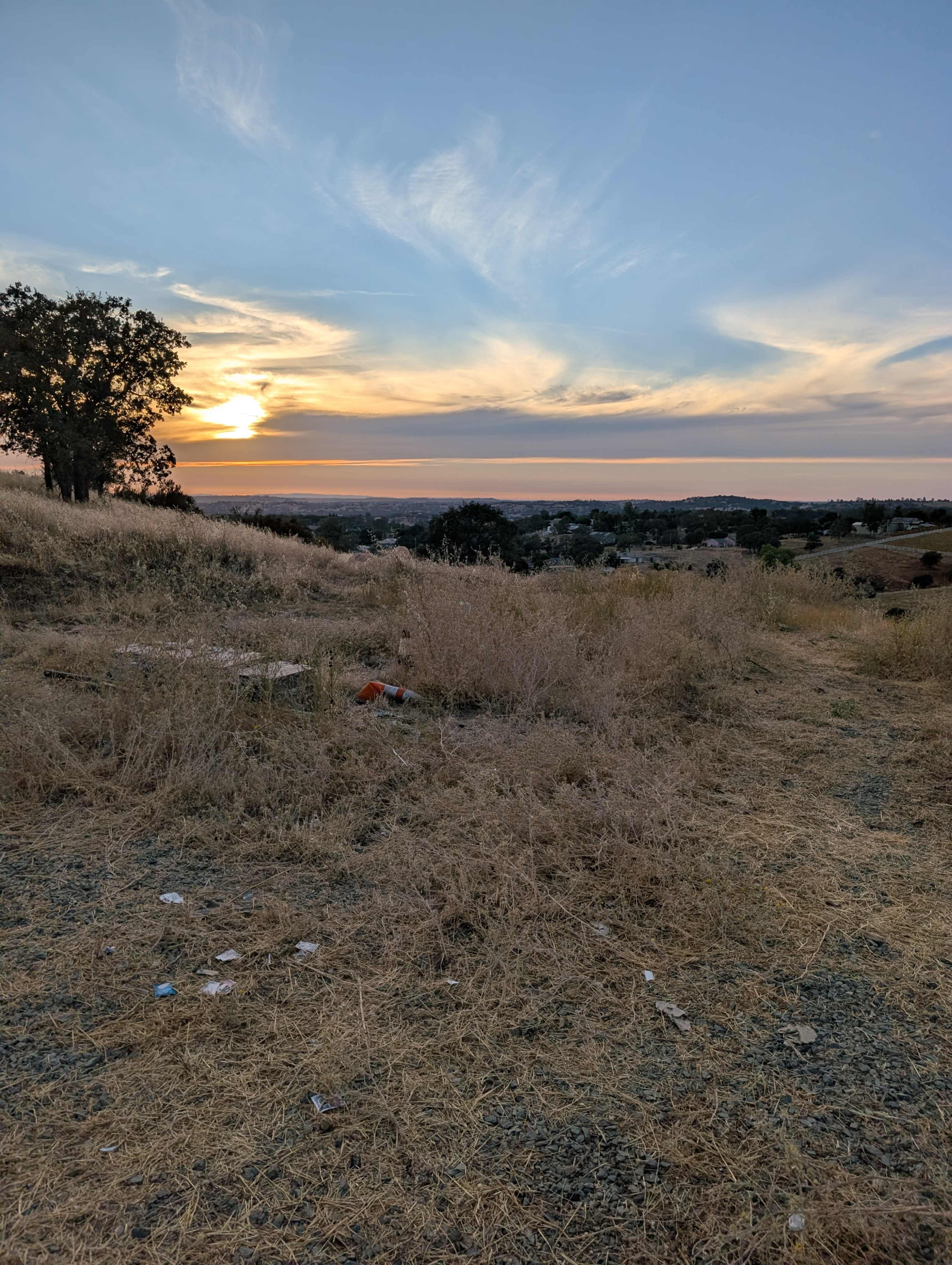 The image shows a grassy hillside at sunset, with a view of the distant landscape and a few scattered bits of litter.