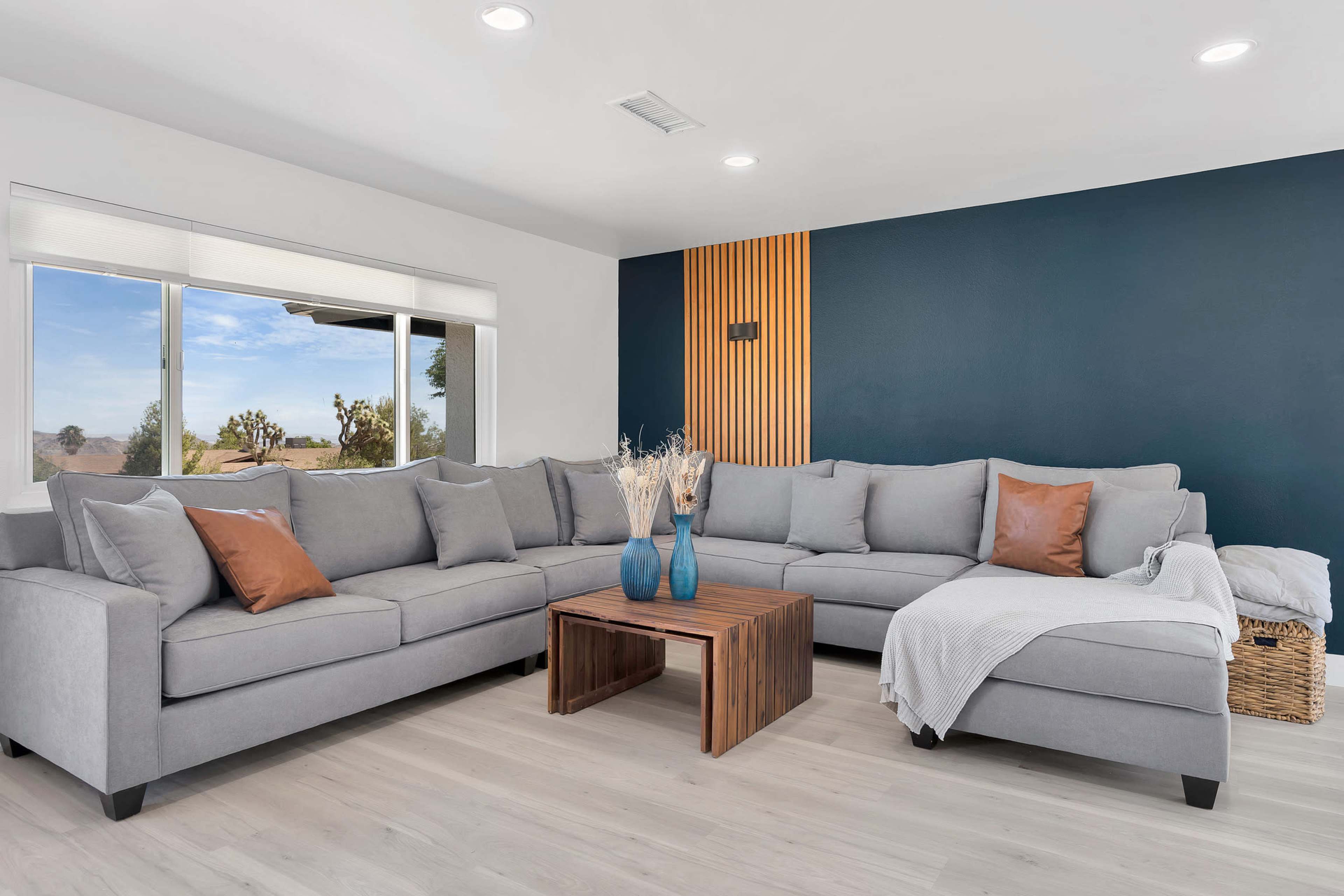 A modern living room featuring a gray sectional sofa, a wooden coffee table, and a textured dark blue accent wall, with natural light coming through a large window.