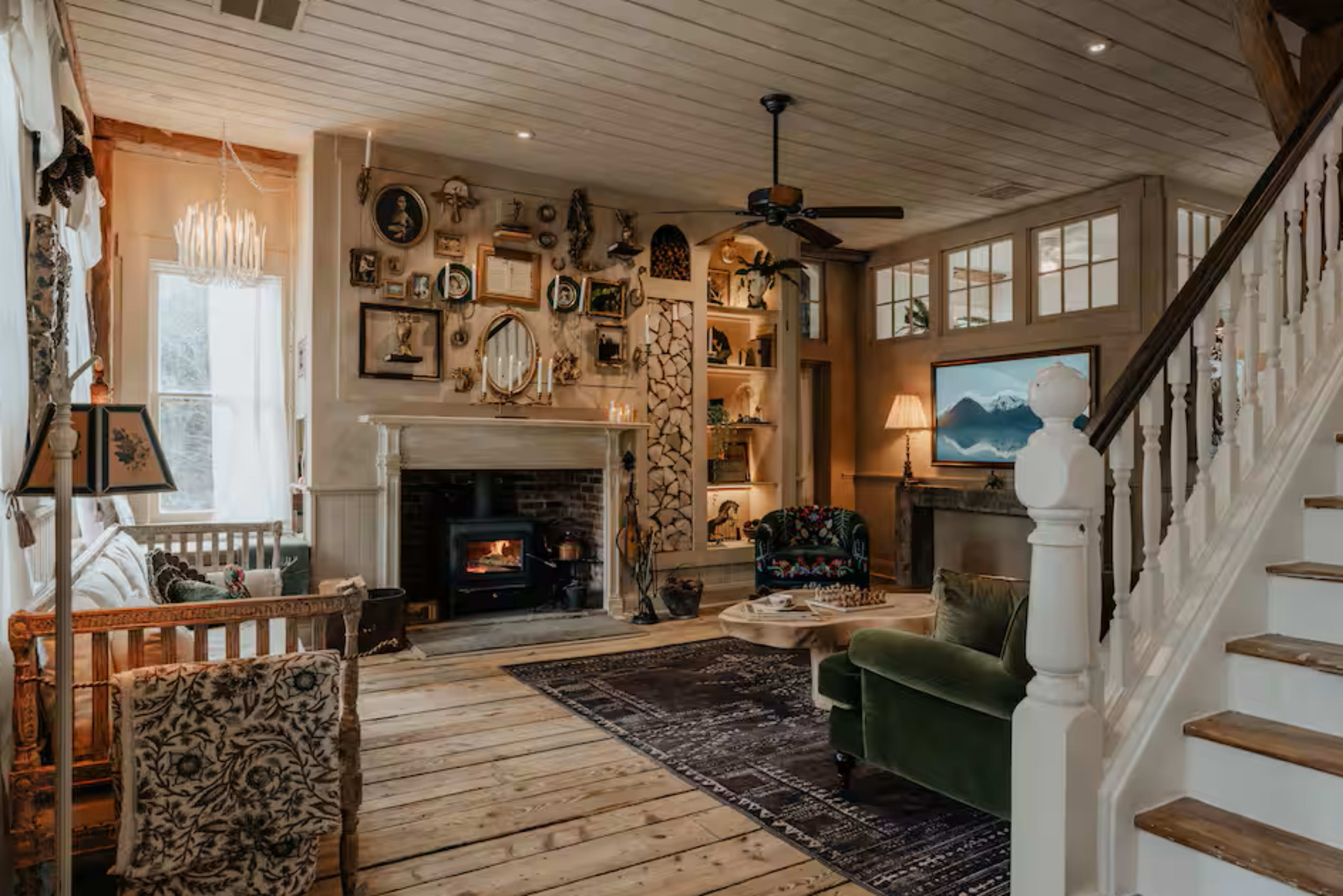 The image depicts a cozy living room with a fireplace, wooden floors, and a mix of decorative items on the walls and shelves.