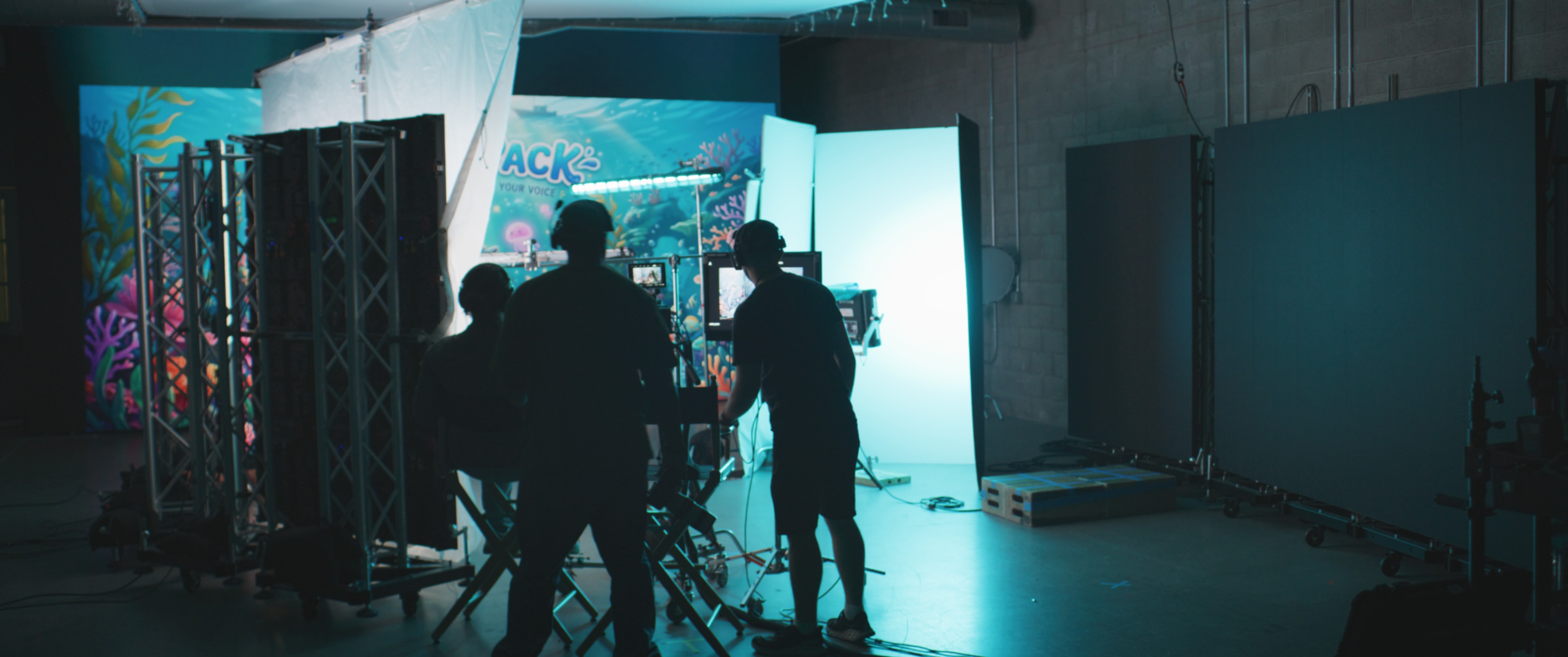 A silhouette of several people is observed in a studio setting with equipment and backdrops arranged for a video or photo shoot.