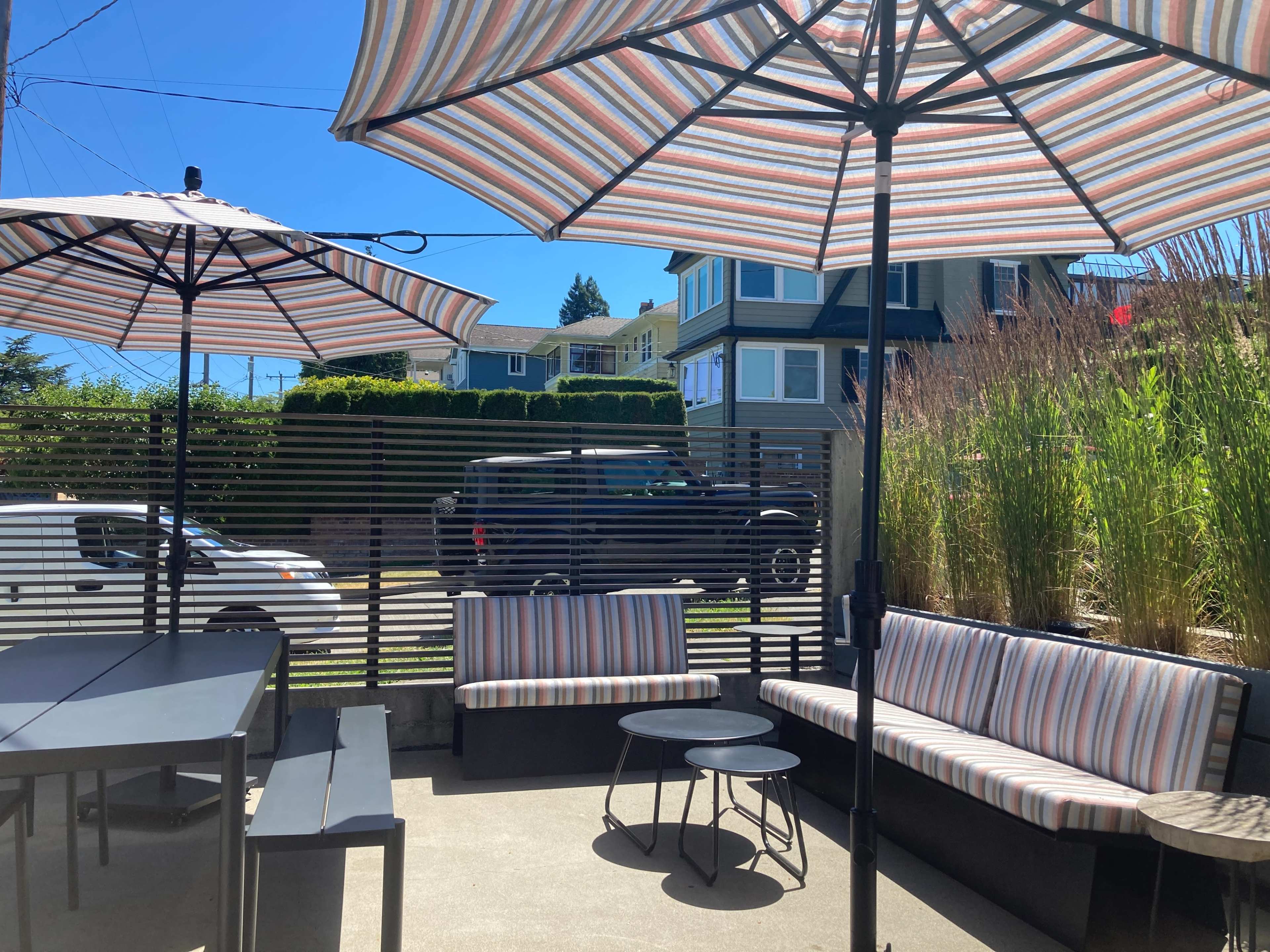 The image shows an outdoor patio area with striped umbrellas, seating, and a view of nearby buildings and a passing vehicle.