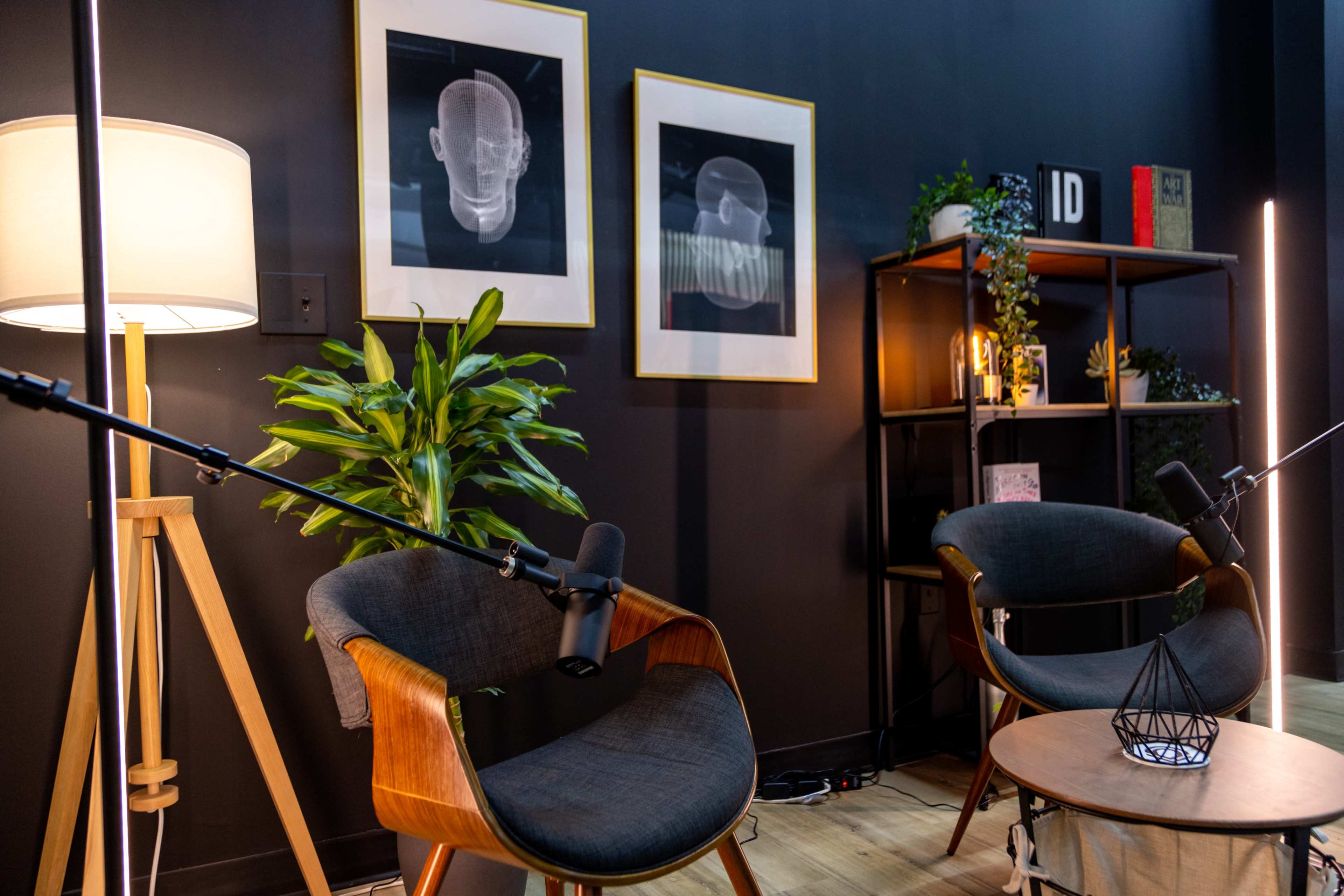 A modern interior featuring two wooden chairs flanking a small coffee table, with a floor lamp and a bookshelf in the background.