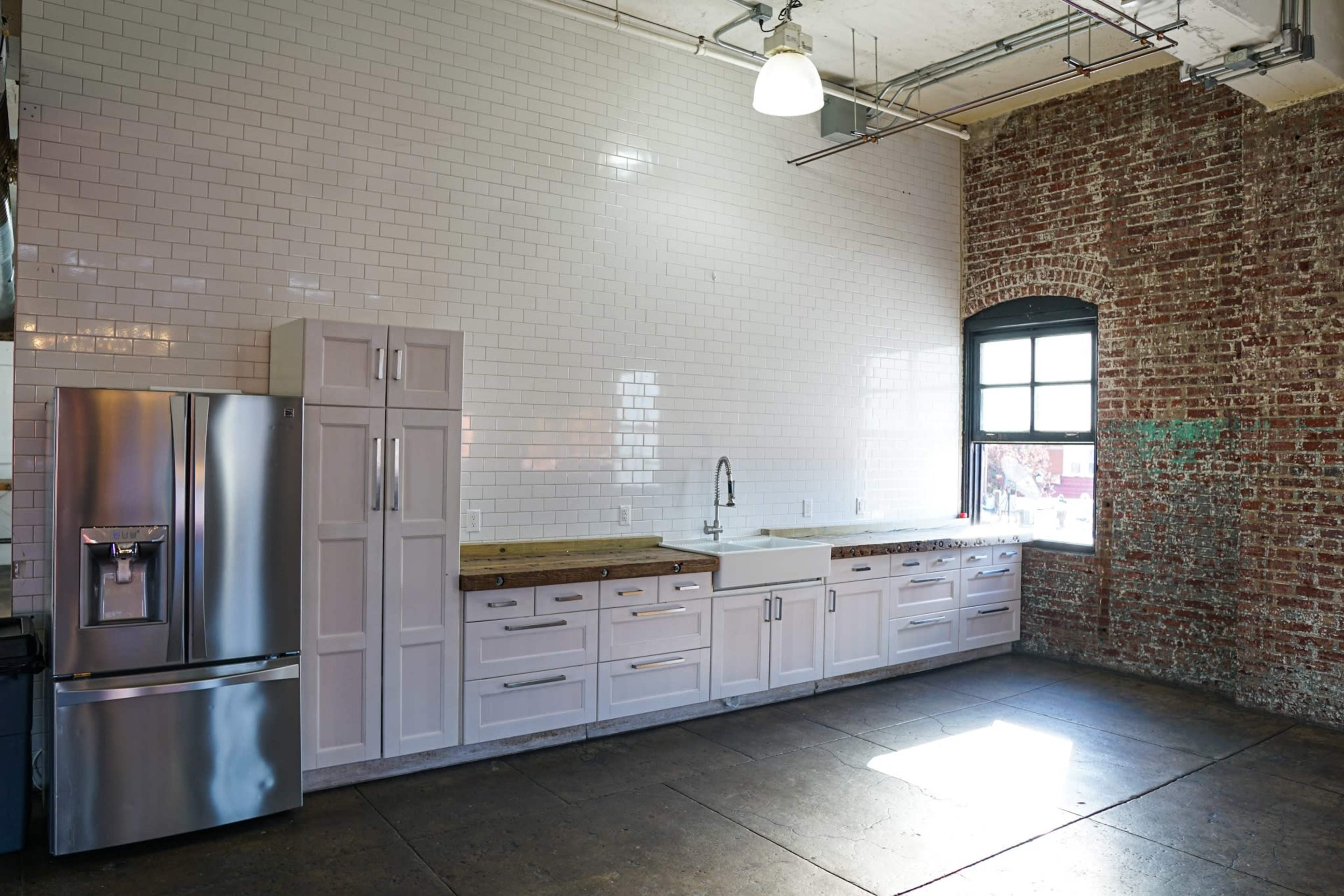 A modern kitchen with stainless steel appliances, white cabinetry, and a brick wall.