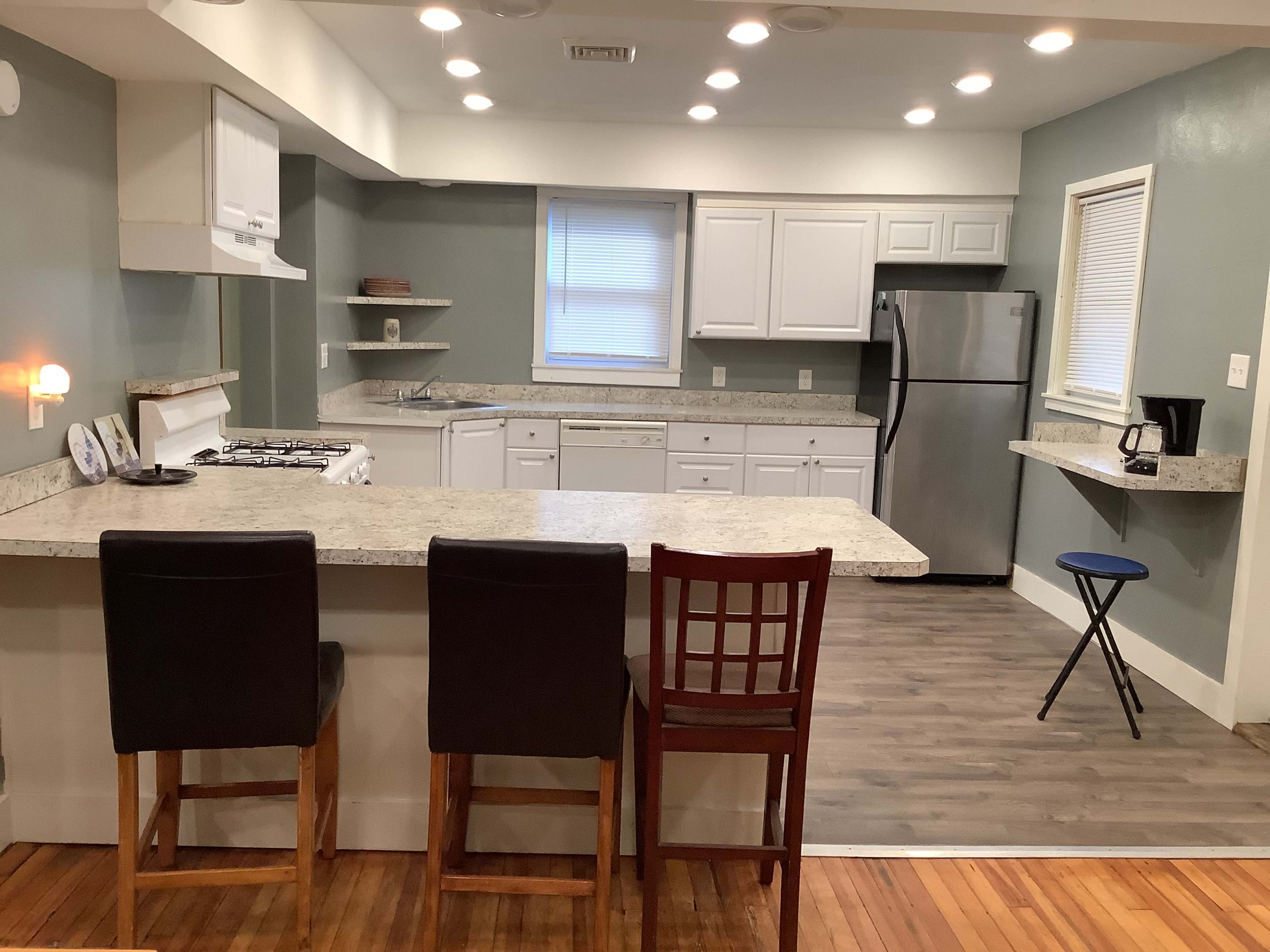 A kitchen with a central island, white cabinetry, stainless steel appliances, and a mix of bar stools and a small chair.