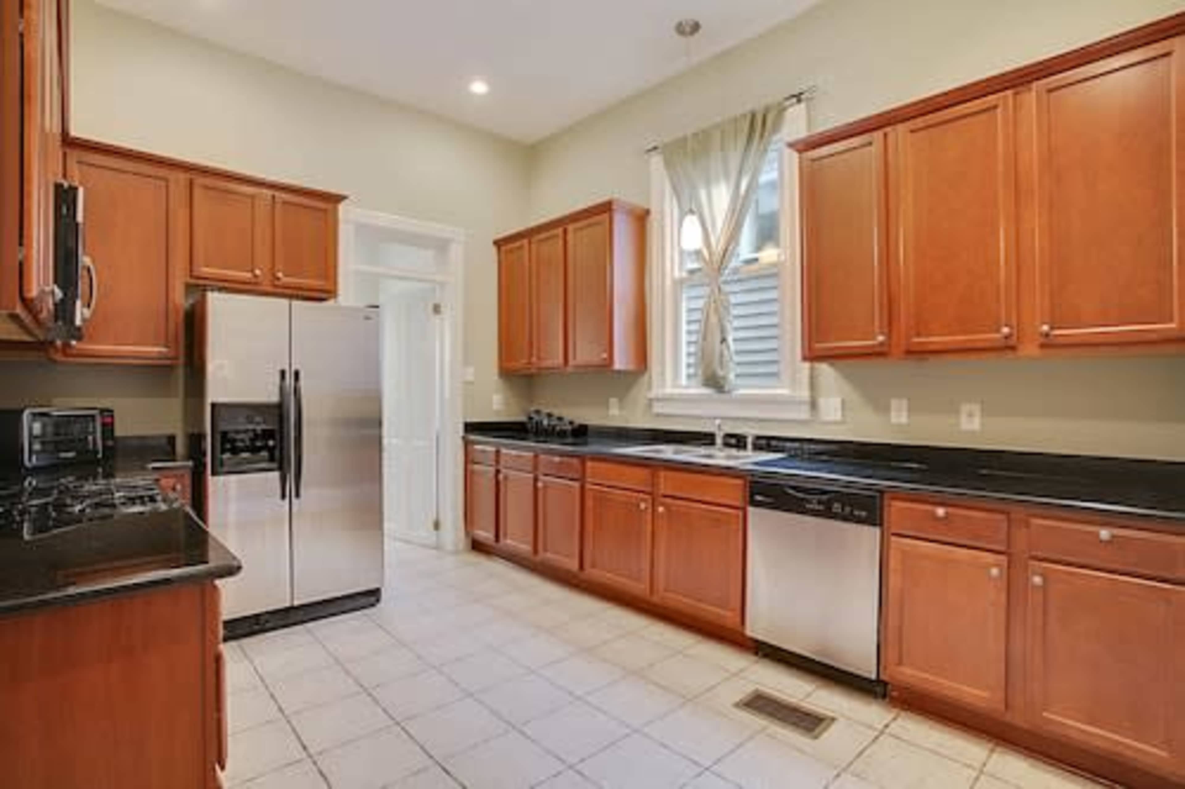 A kitchen with wooden cabinets, stainless steel appliances, and a tiled floor.