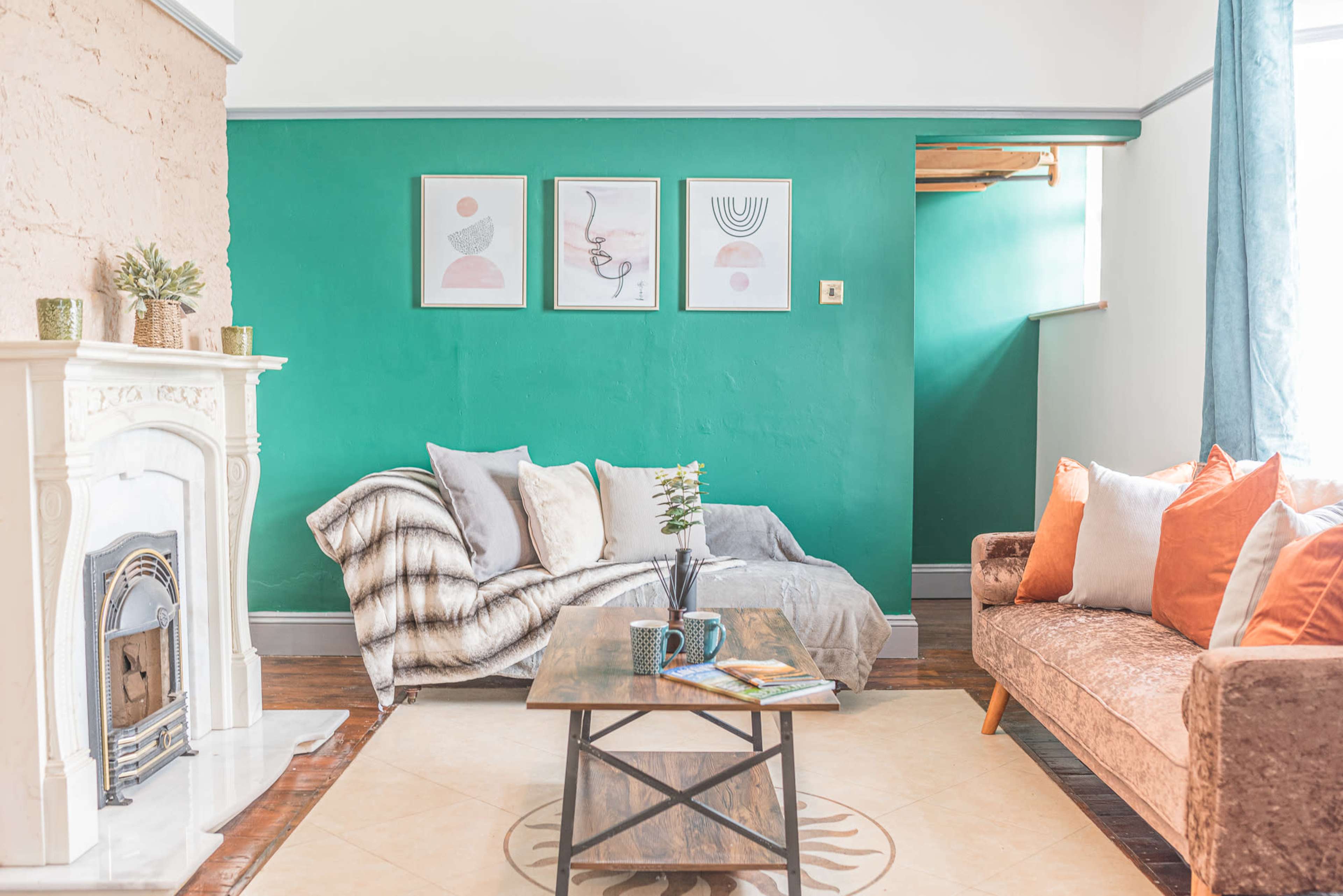 A cozy living room featuring a teal accent wall, a white fireplace, a brown sofa, and a coffee table with a mug and book on it.