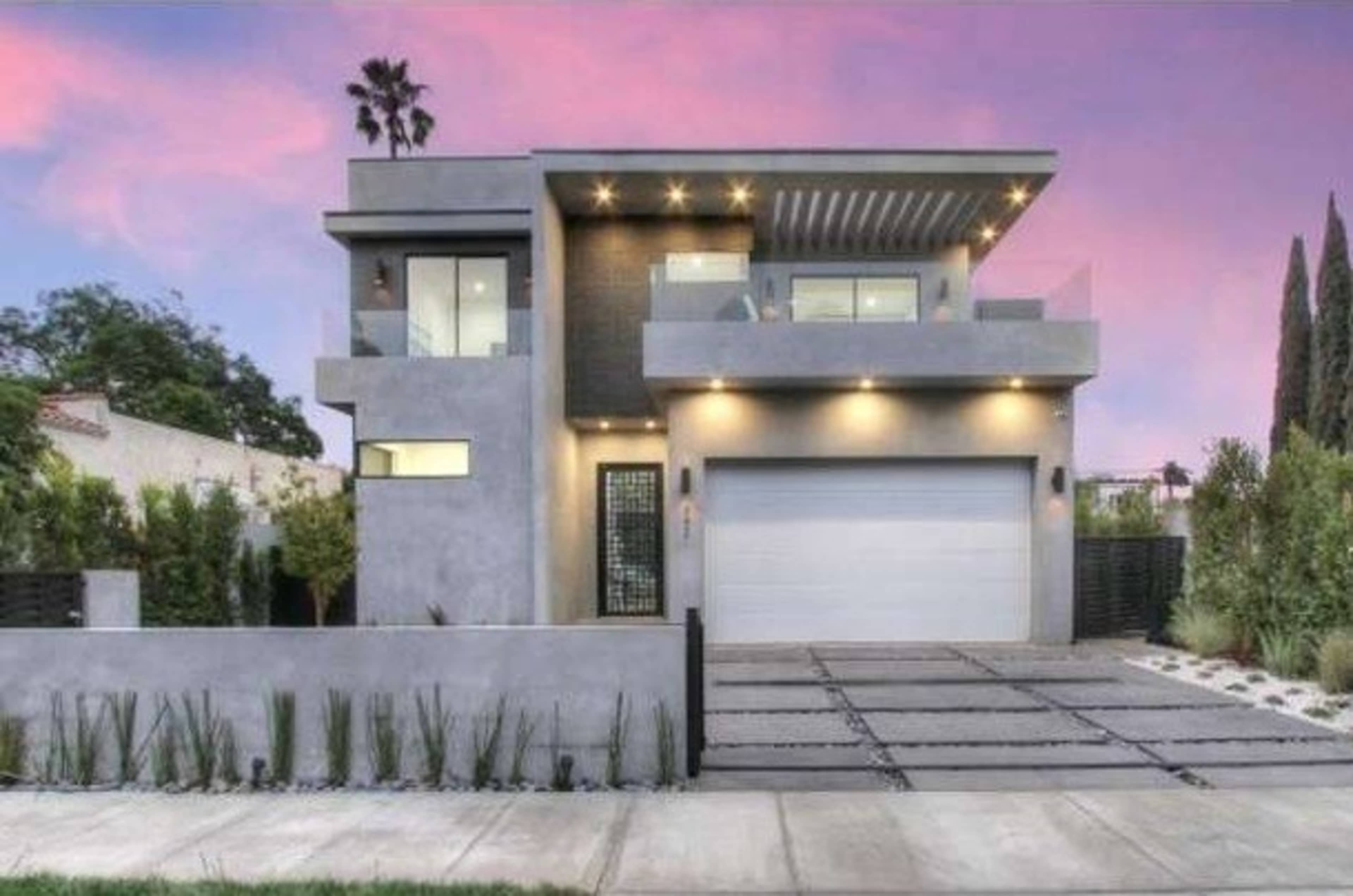 A modern two-story house with a gray exterior, large windows, and a driveway lined with stone pavers.