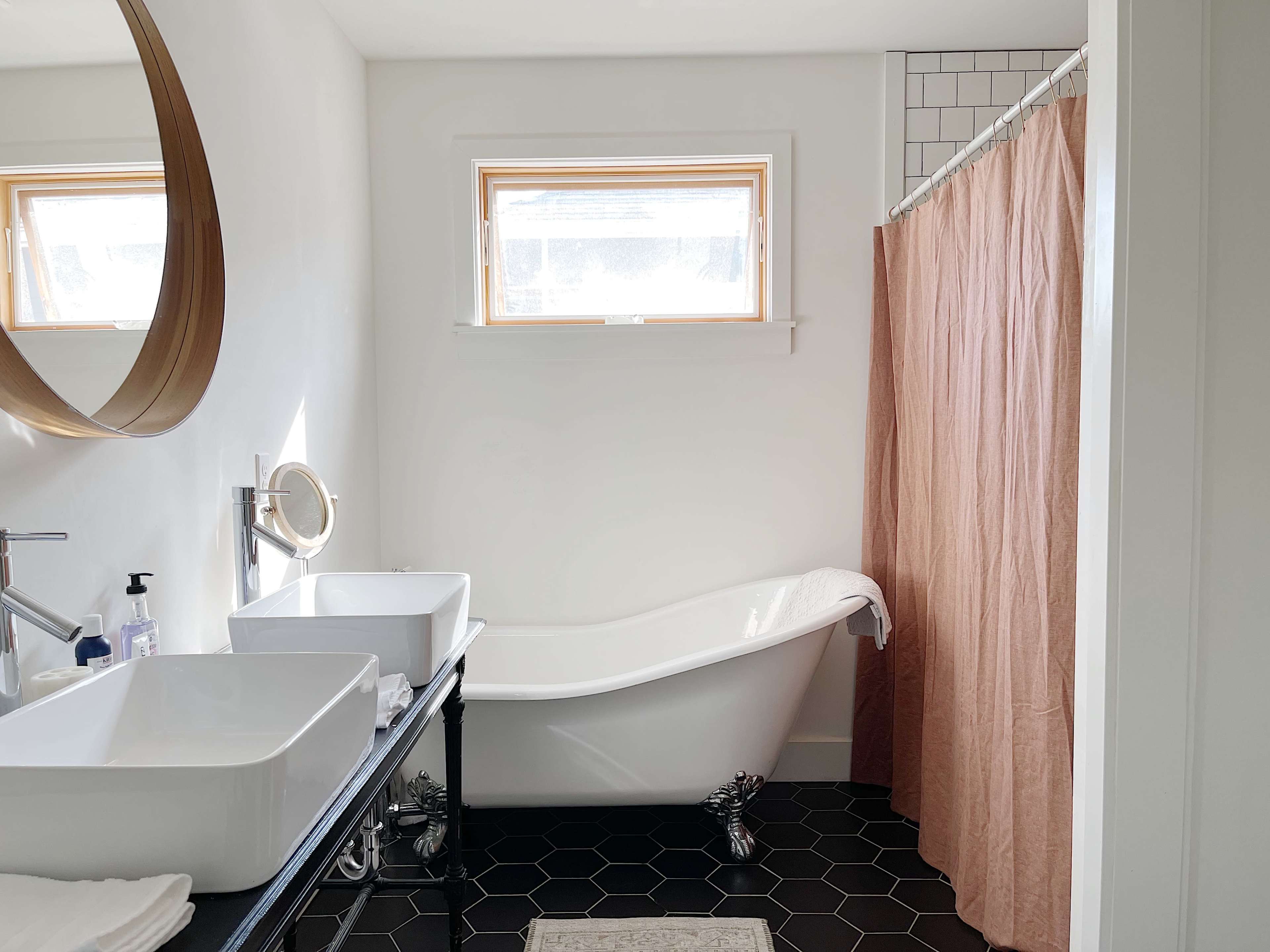 The image shows a modern bathroom featuring a freestanding bathtub, a double sink vanity, and a light-colored shower curtain.