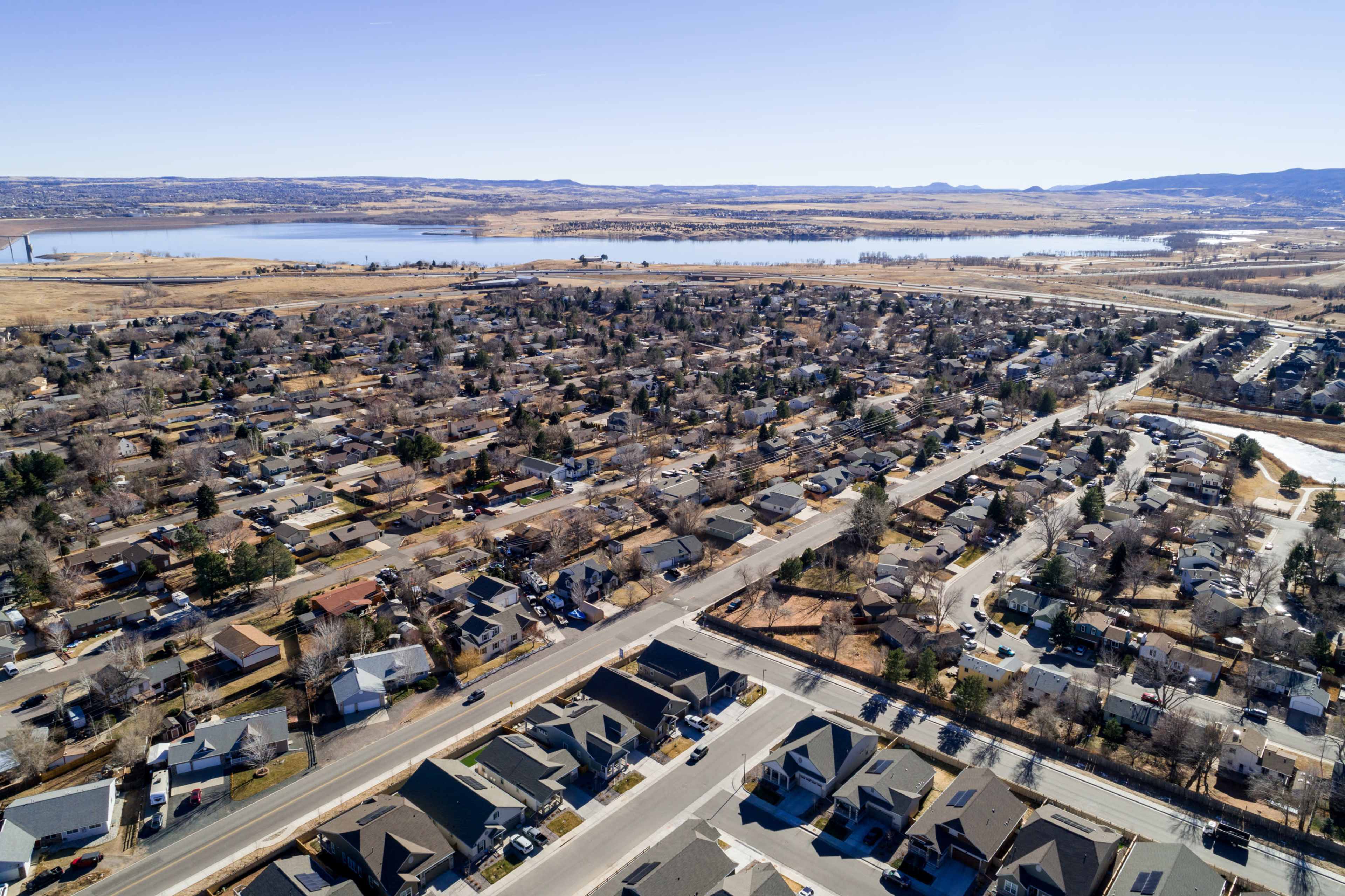An aerial view of a suburban neighborhood with rows of houses and a nearby body of water under clear skies.