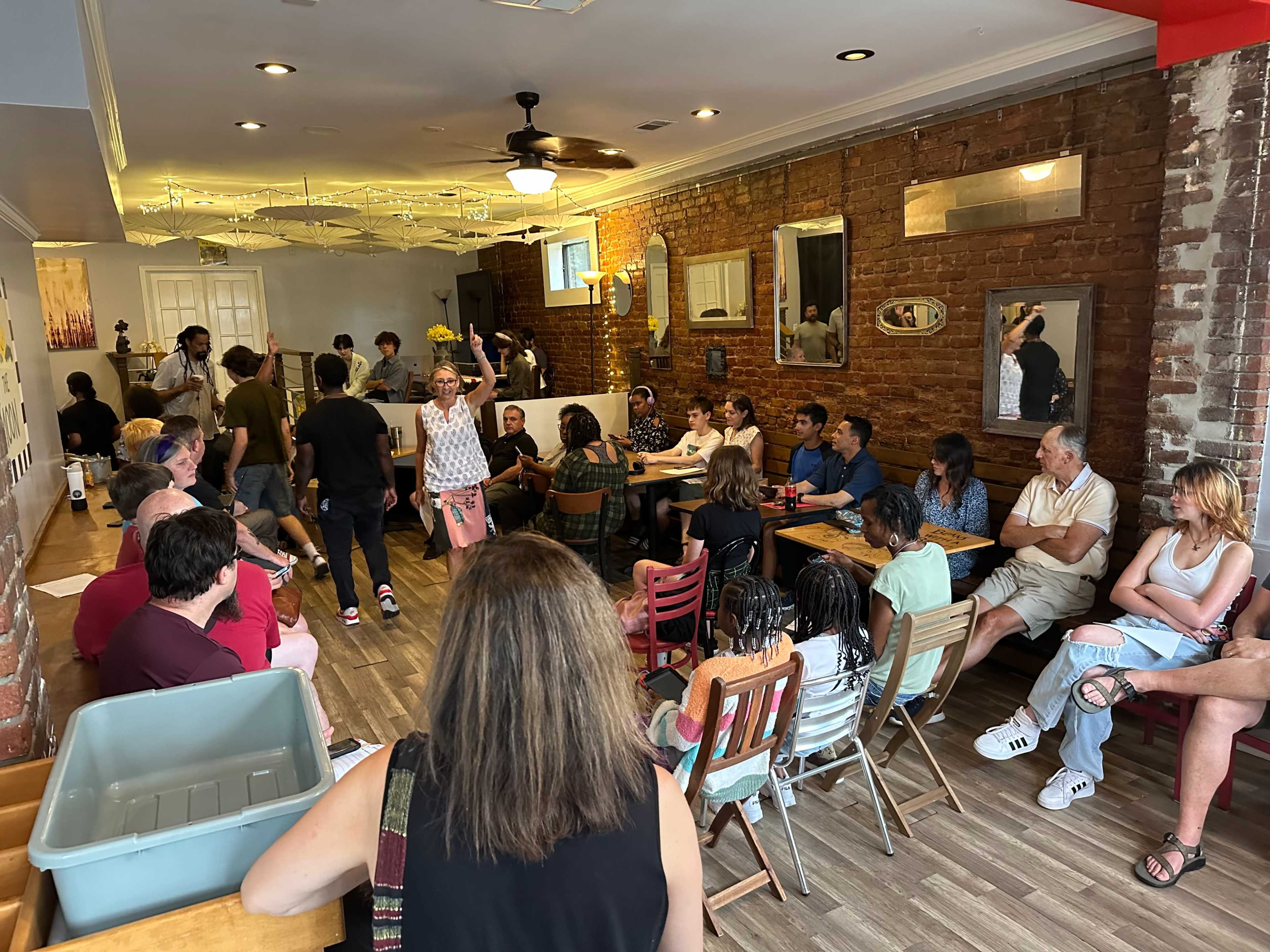 A diverse group of people is seated at various tables in a restaurant with exposed brick walls and a wooden floor.