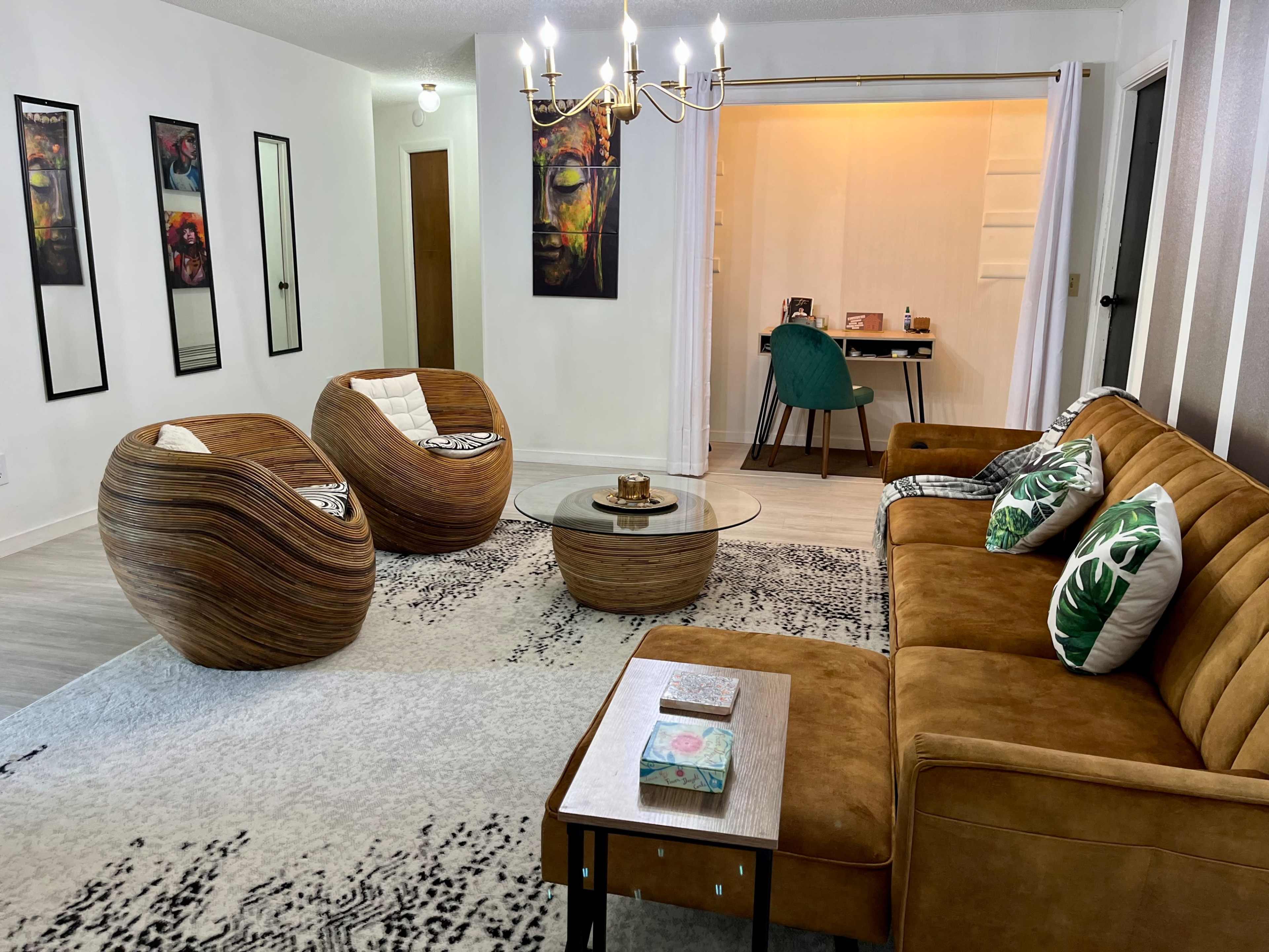 A modern living room with two curved wicker chairs, a glass coffee table, and a brown sofa, arranged around a rug with a dark pattern.