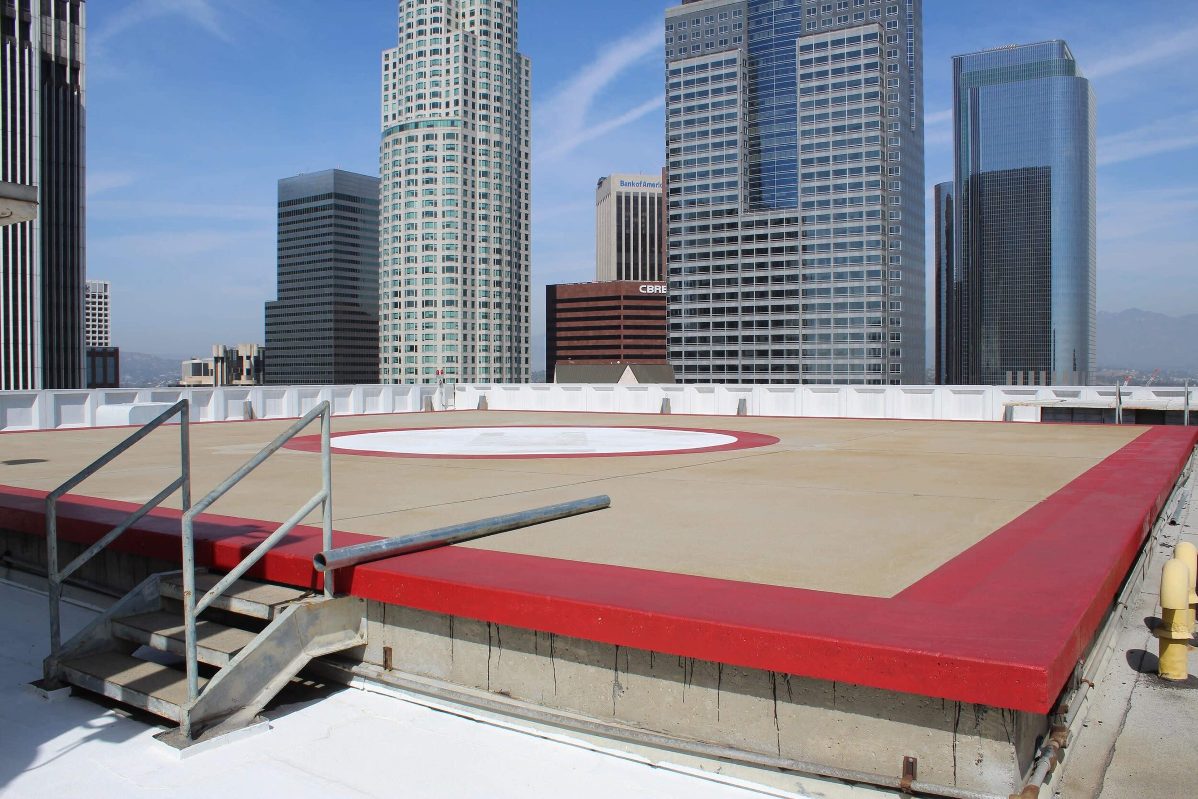 A rooftop helicopter pad is surrounded by tall buildings in a city skyline.