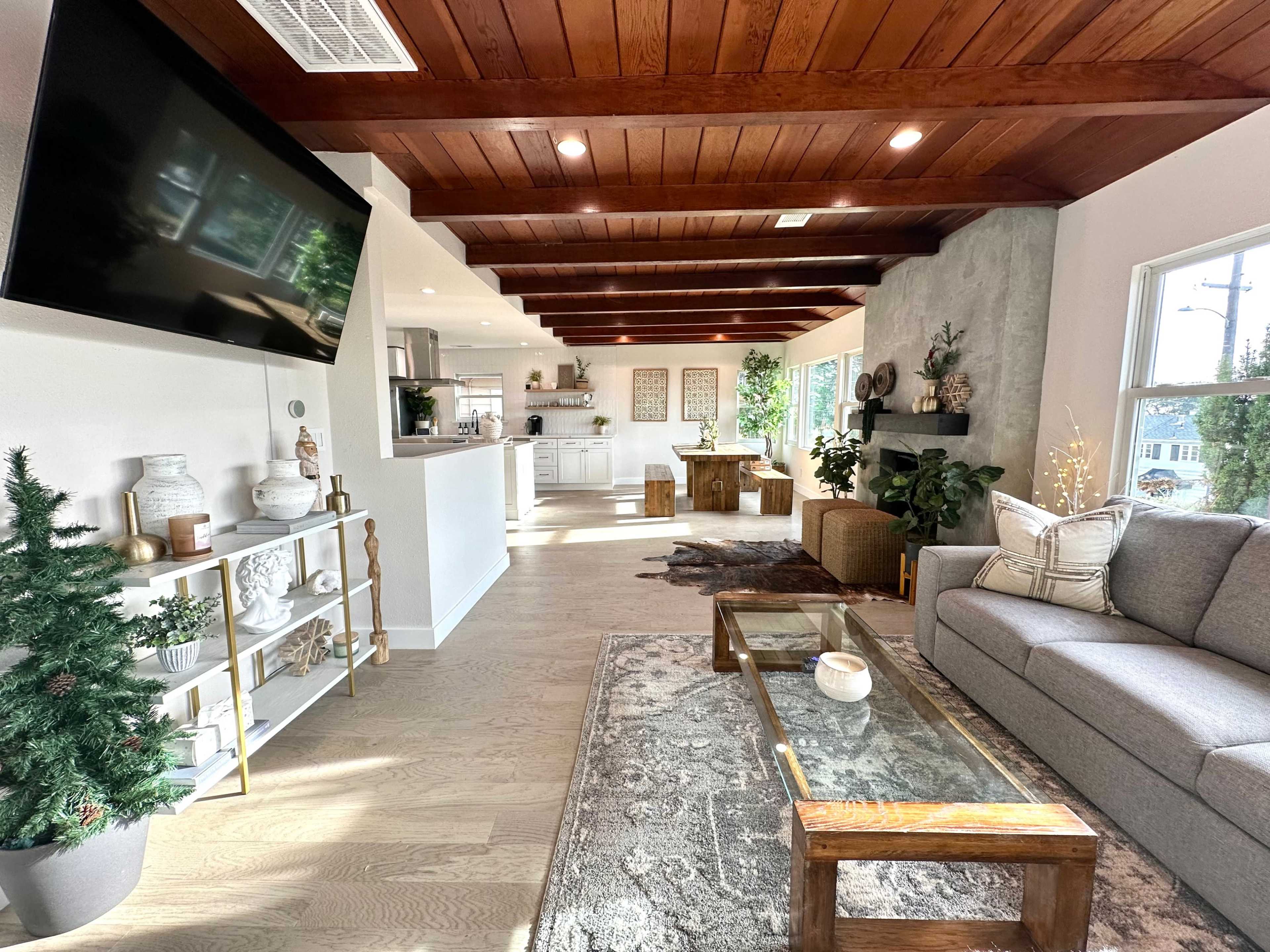 A modern living room with a gray sofa, a wooden coffee table, and an open layout featuring a kitchen area in the background, all illuminated by natural light.